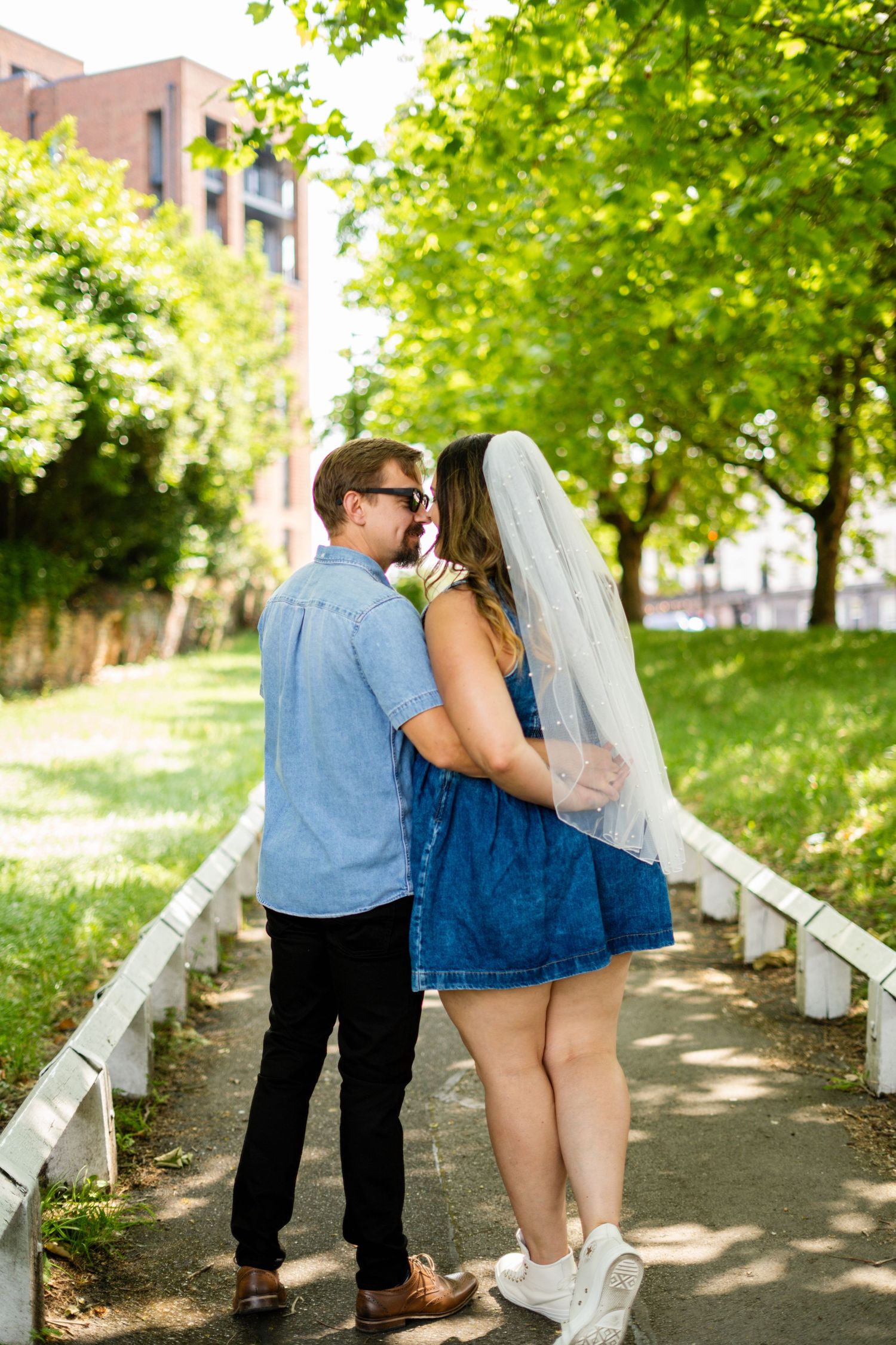 A couple sharing an intimate moment on a pathway surrounded by green trees.