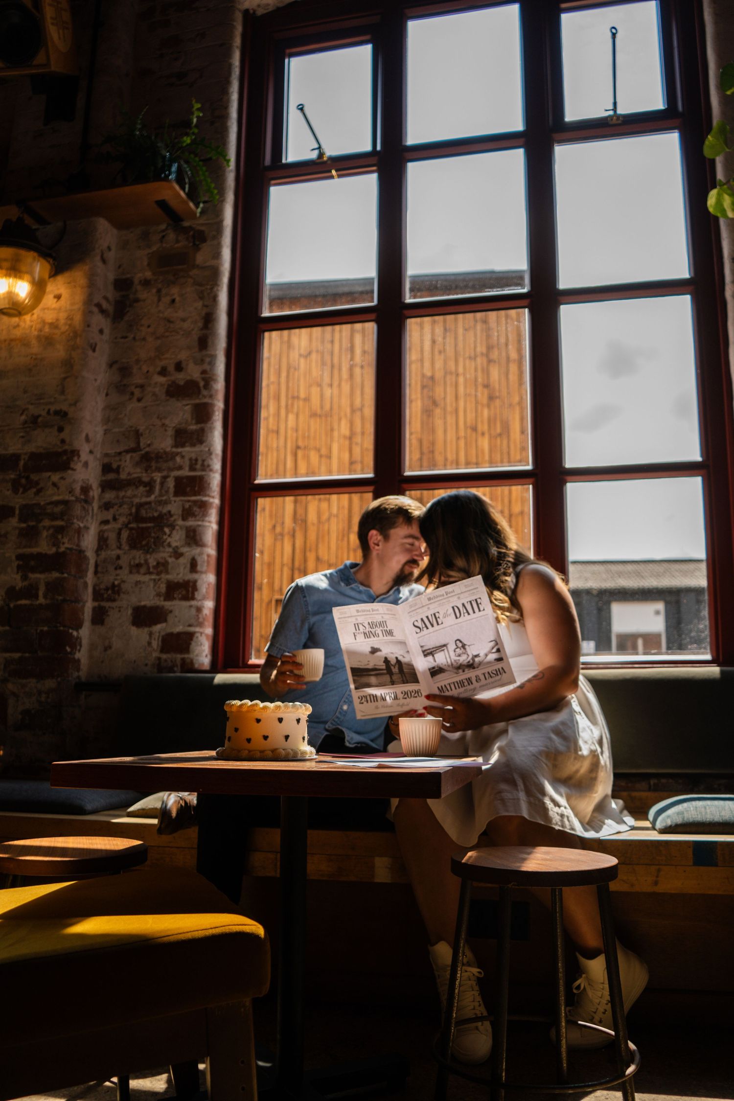 A couple sits in dramatic lighting by large windows in an industrial space.
