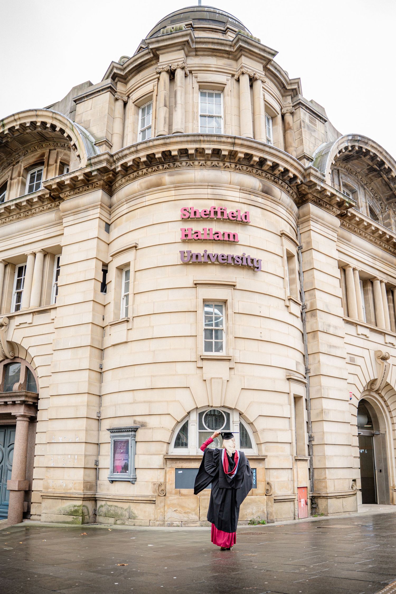Wide angle view of graduate posing in front of ornate stone building facade.