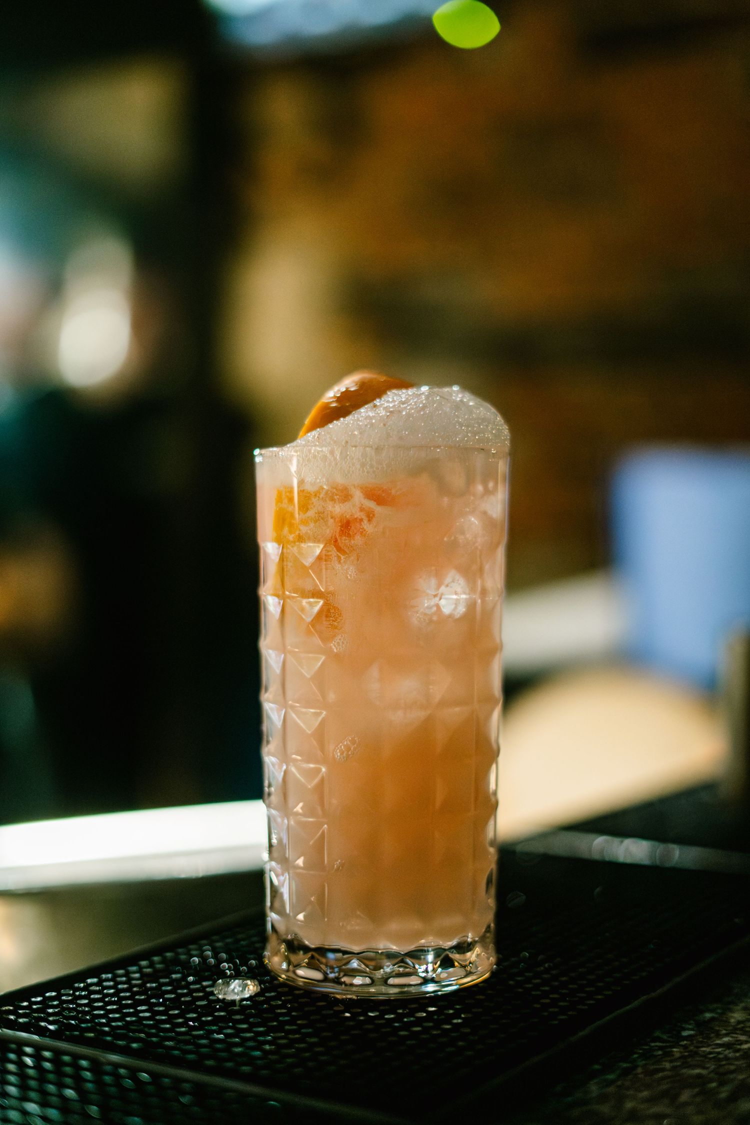 Pink cocktail in a cut crystal glass sitting on a black bar mat.
