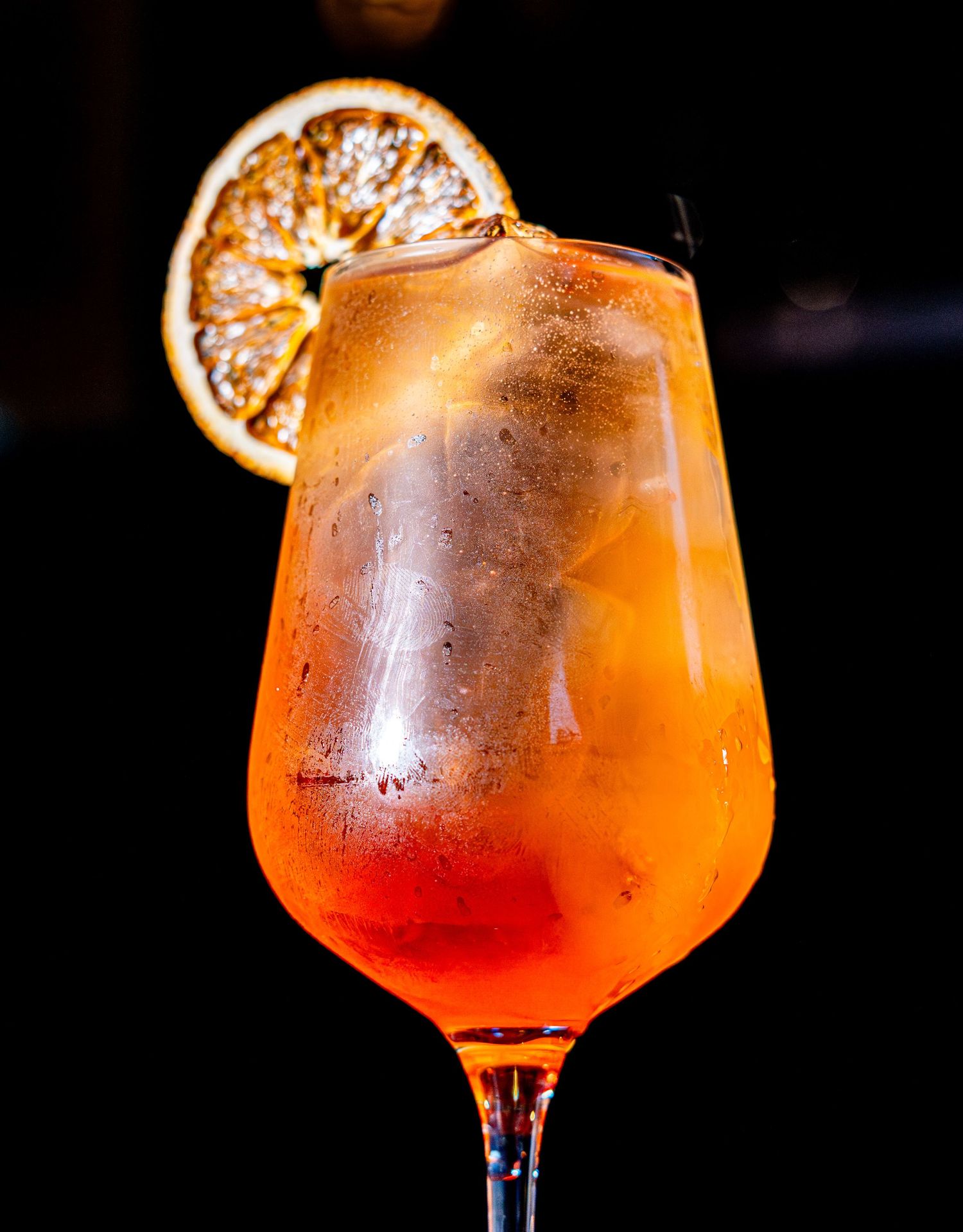 An orange cocktail garnished with a dried citrus wheel in a stemmed glass.