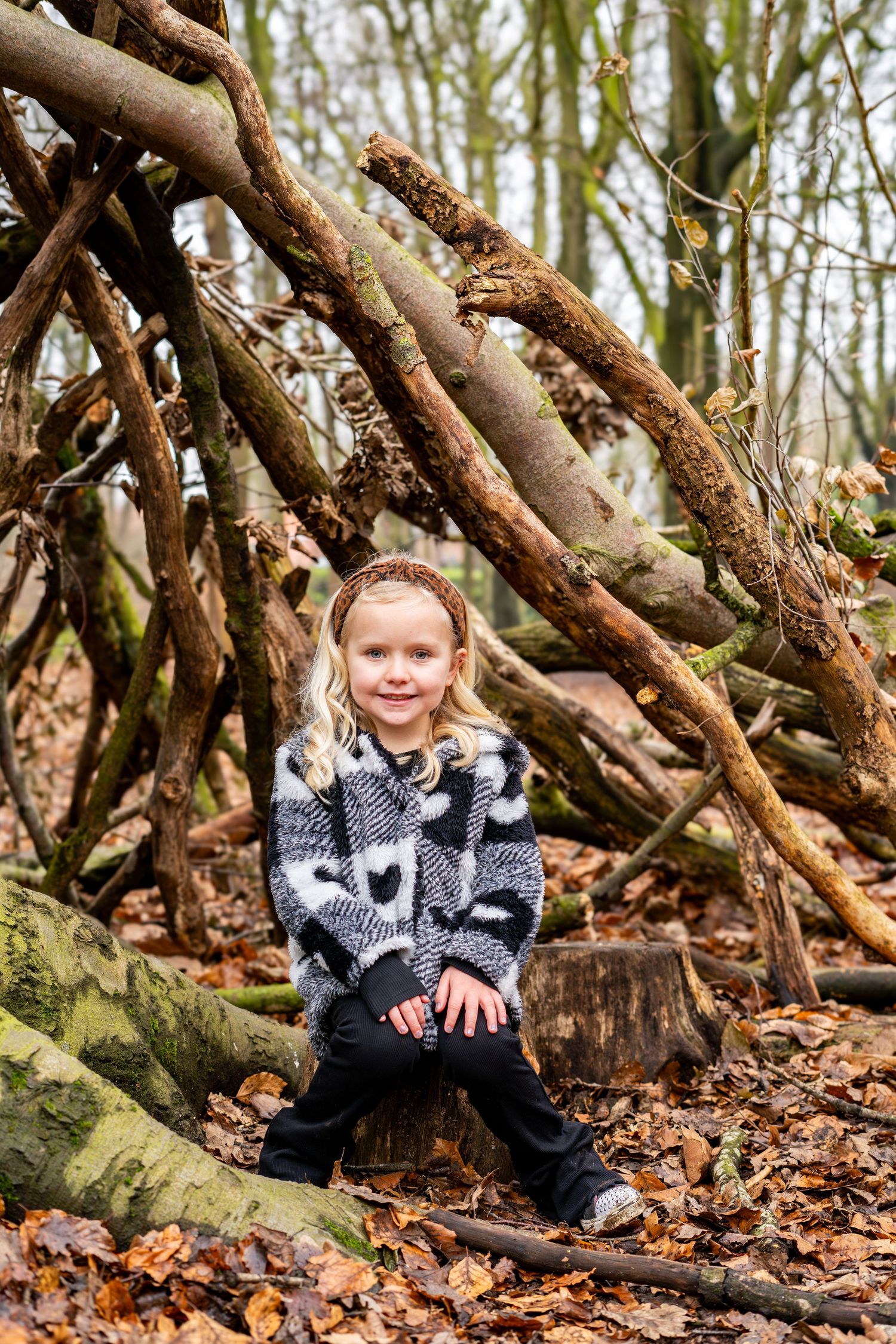 Child sitting among fallen branches and autumn leaves in the woods.