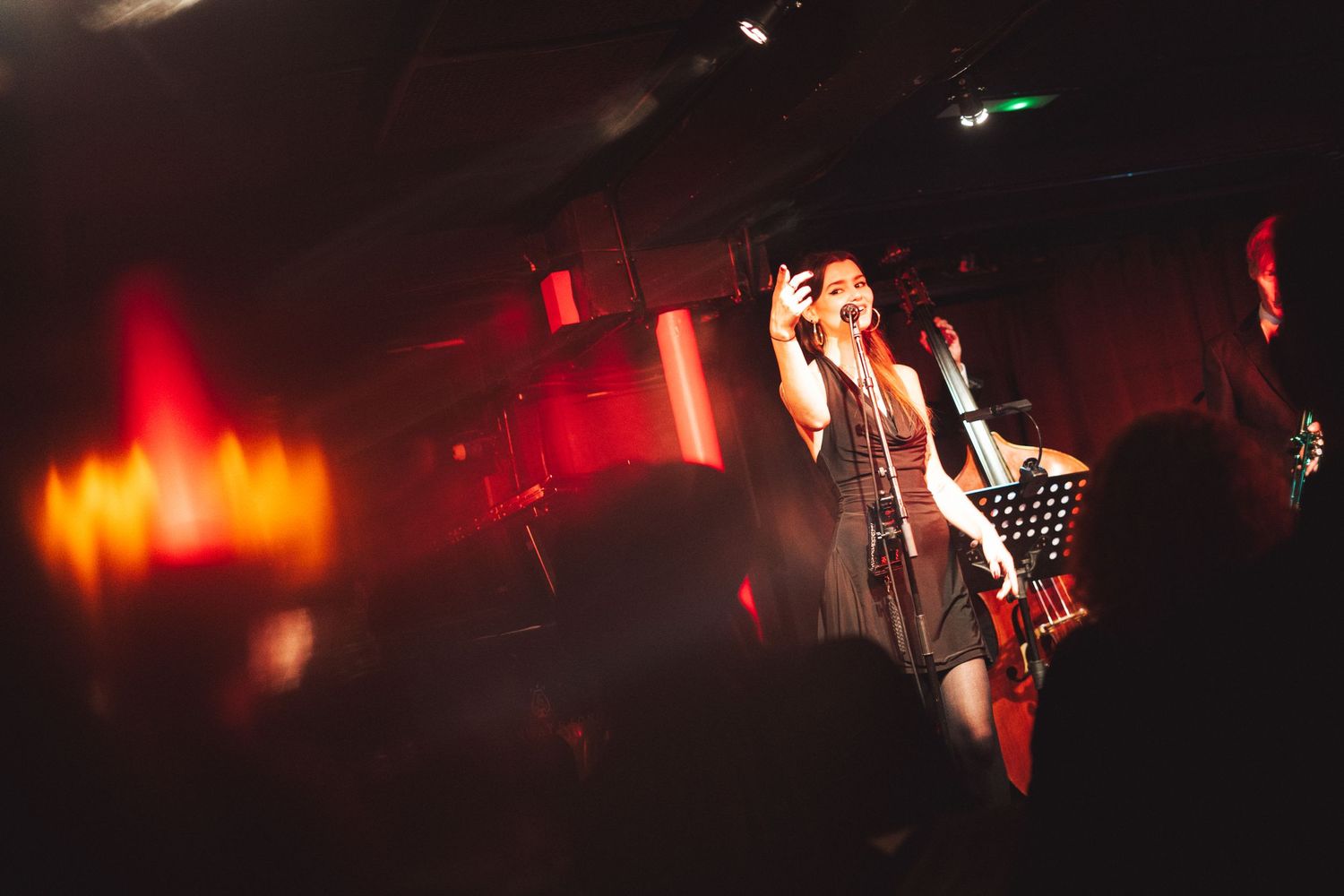 Concert venue bathed in dramatic red stage lighting with silhouettes visible in the darkness.