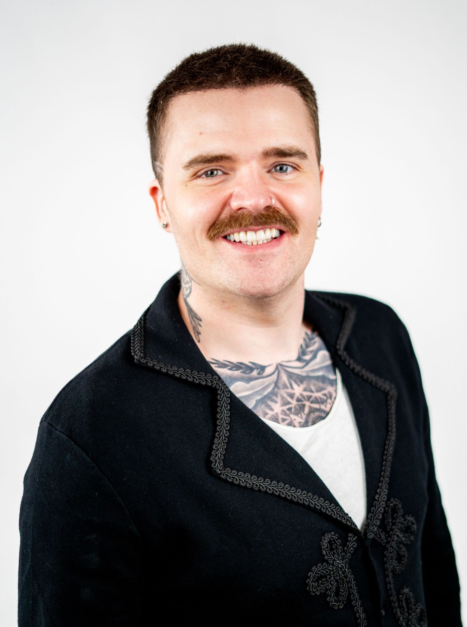 Studio portrait of a person with a mustache wearing a black textured jacket.