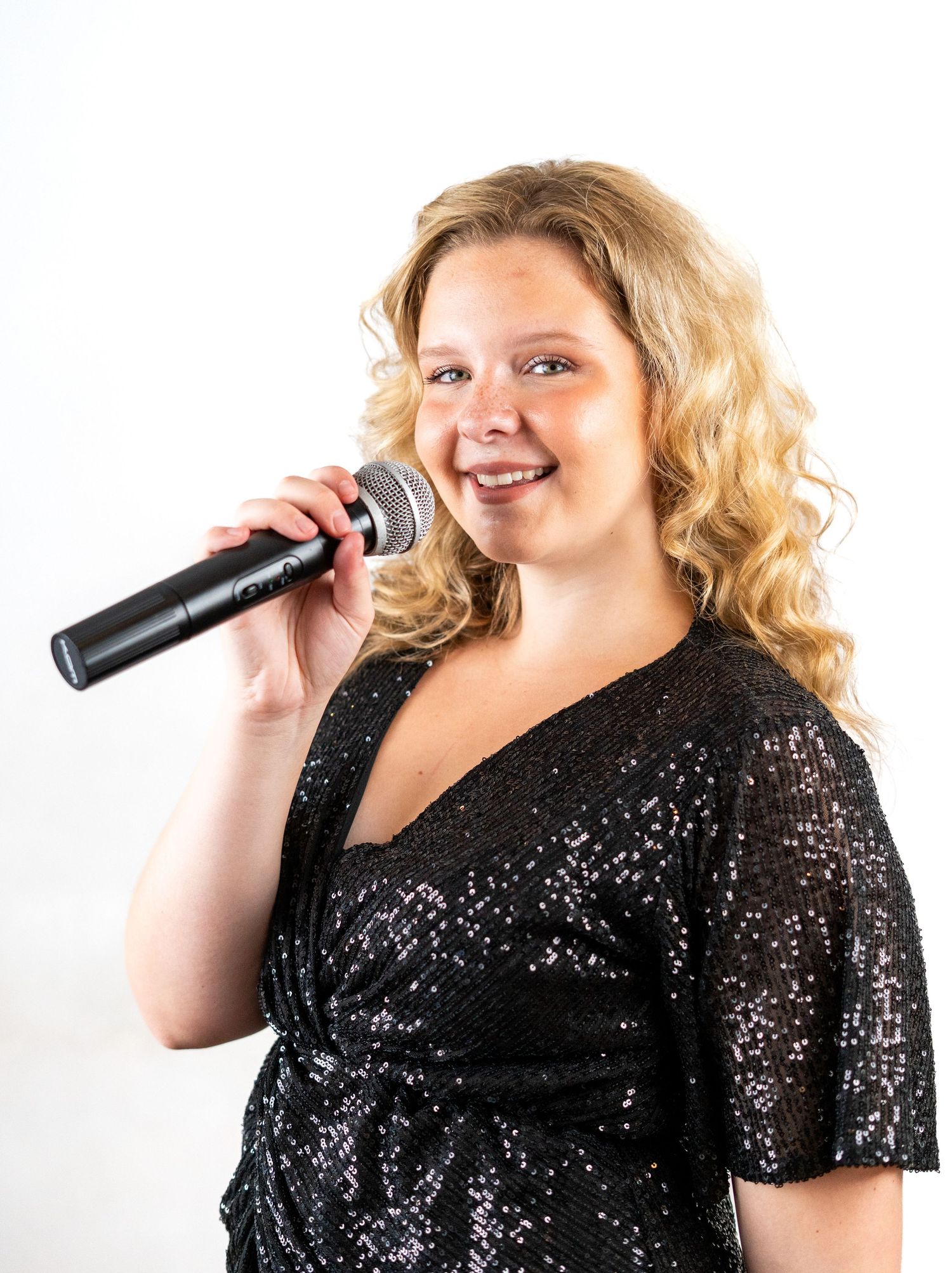 Singer wearing a glittery black outfit performs with a handheld microphone.