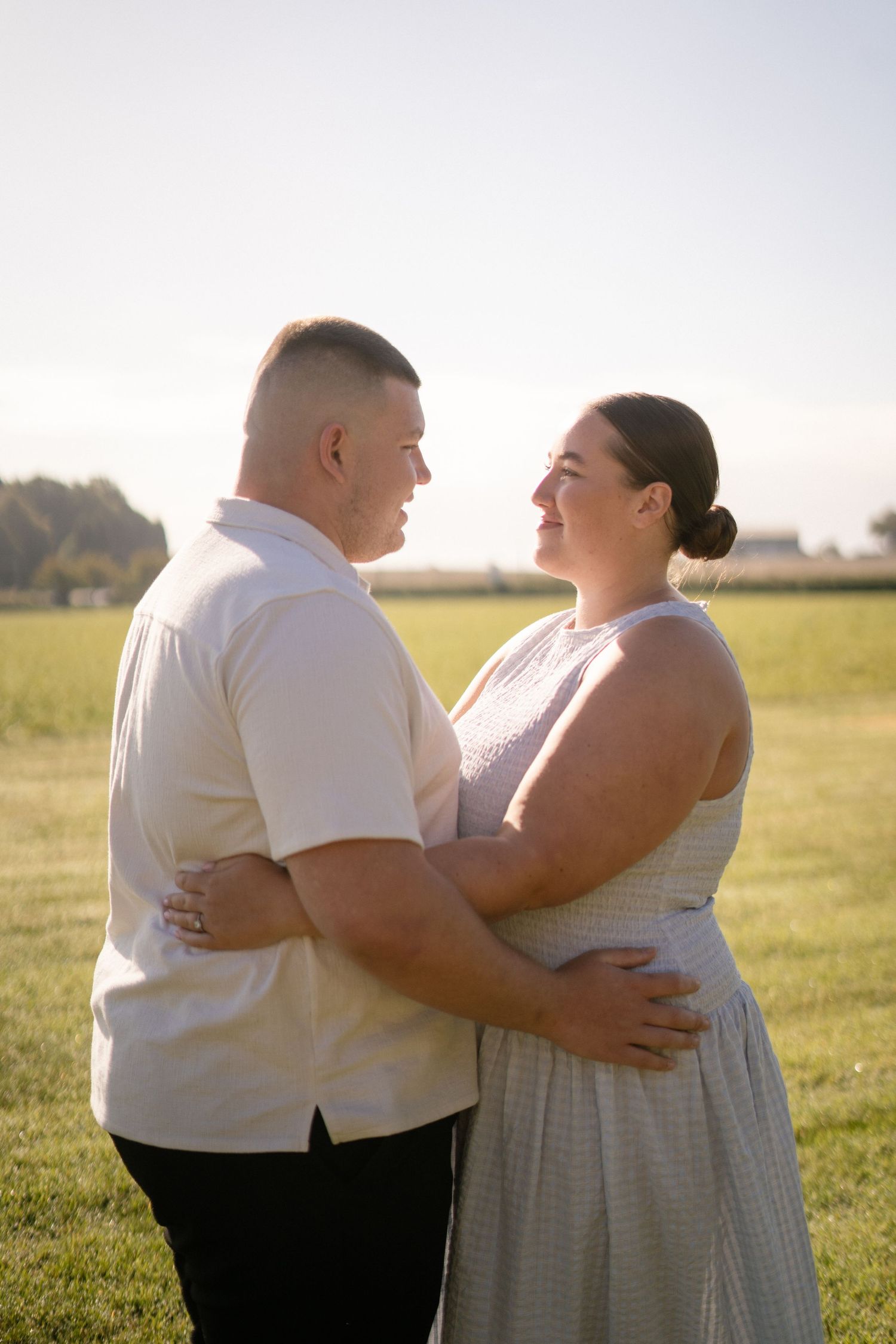 Couple embracing in a sunlit field wearing white and cream colored outfits.