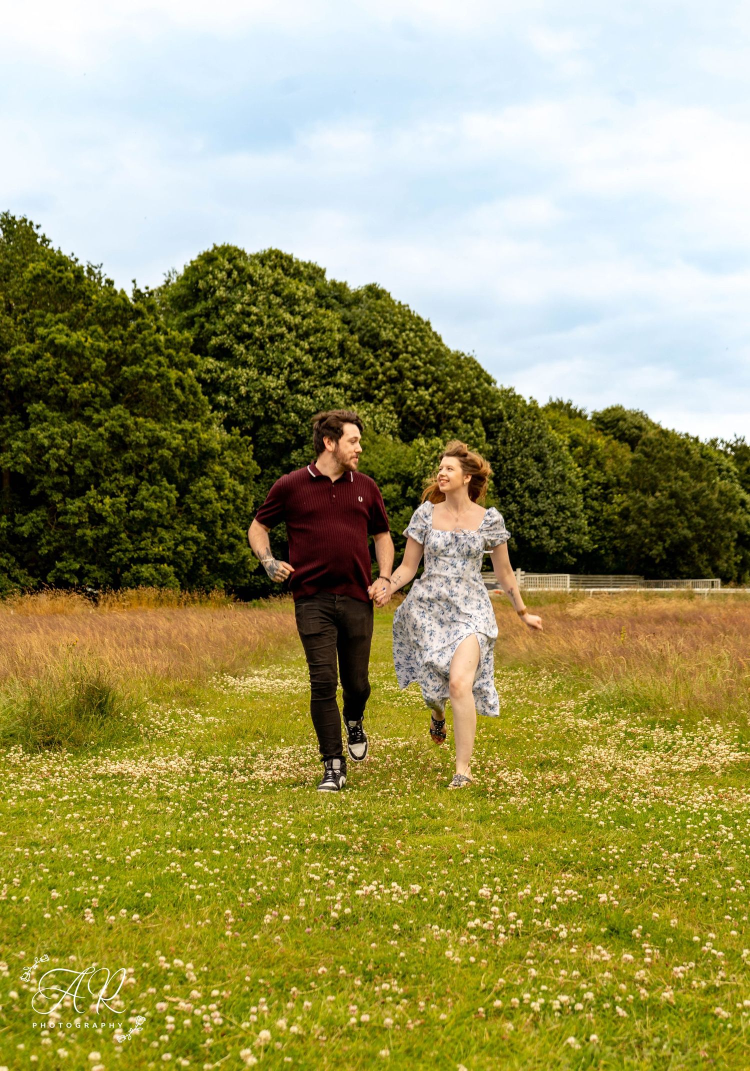 A couple walks playfully through a wildflower meadow on a summer day.