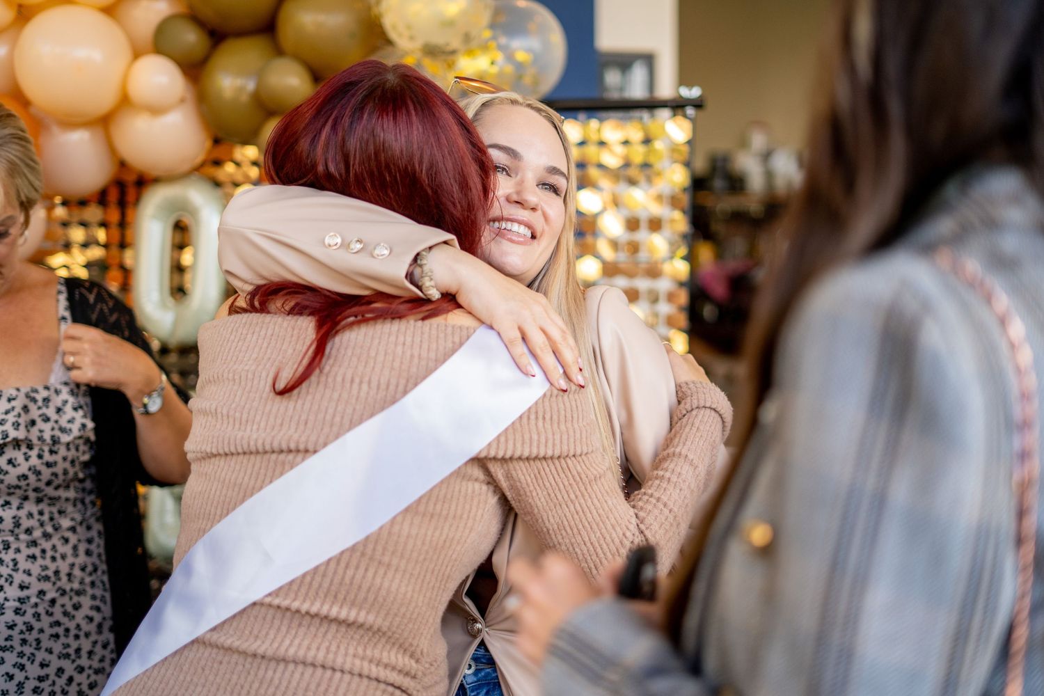 Candid moments of celebration captured with friends hugging against festive balloon backdrop.