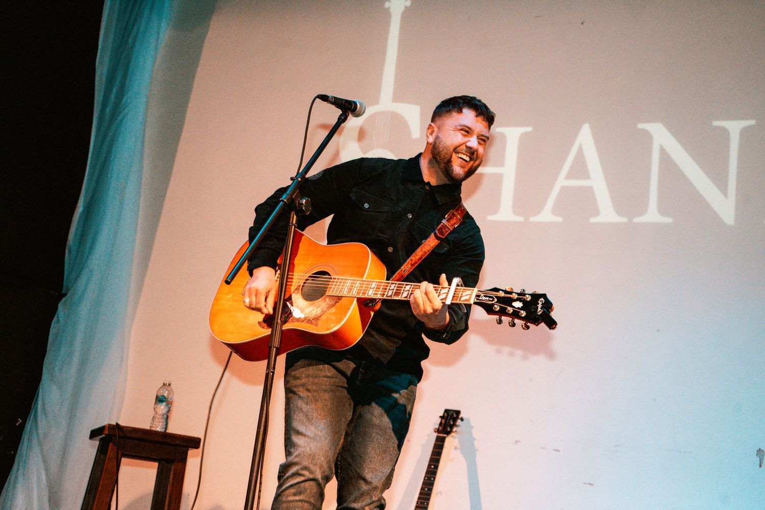A musician performs with an acoustic guitar on stage under soft lighting.
