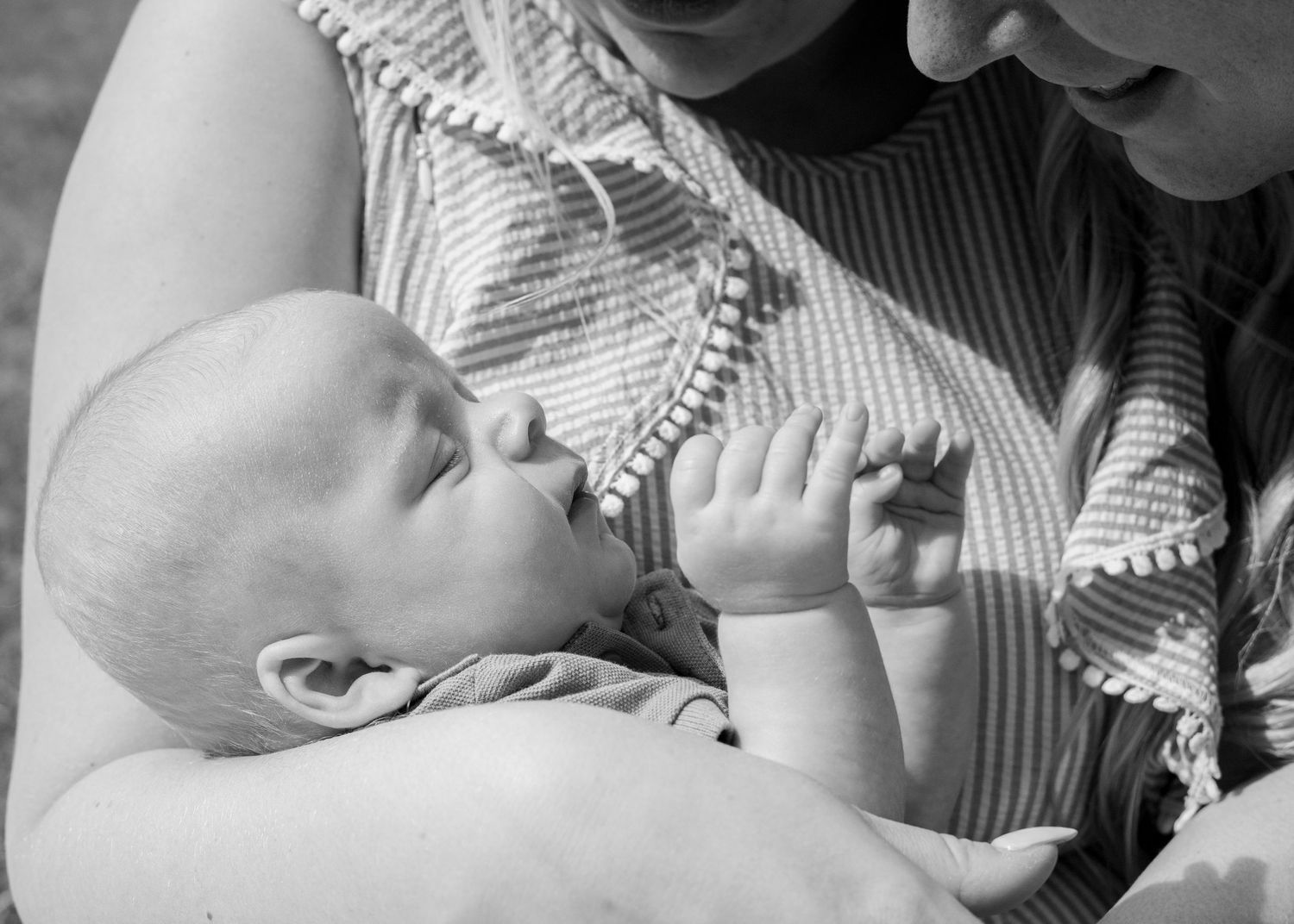 Black and white portrait of an infant being tenderly held in striped fabric.
