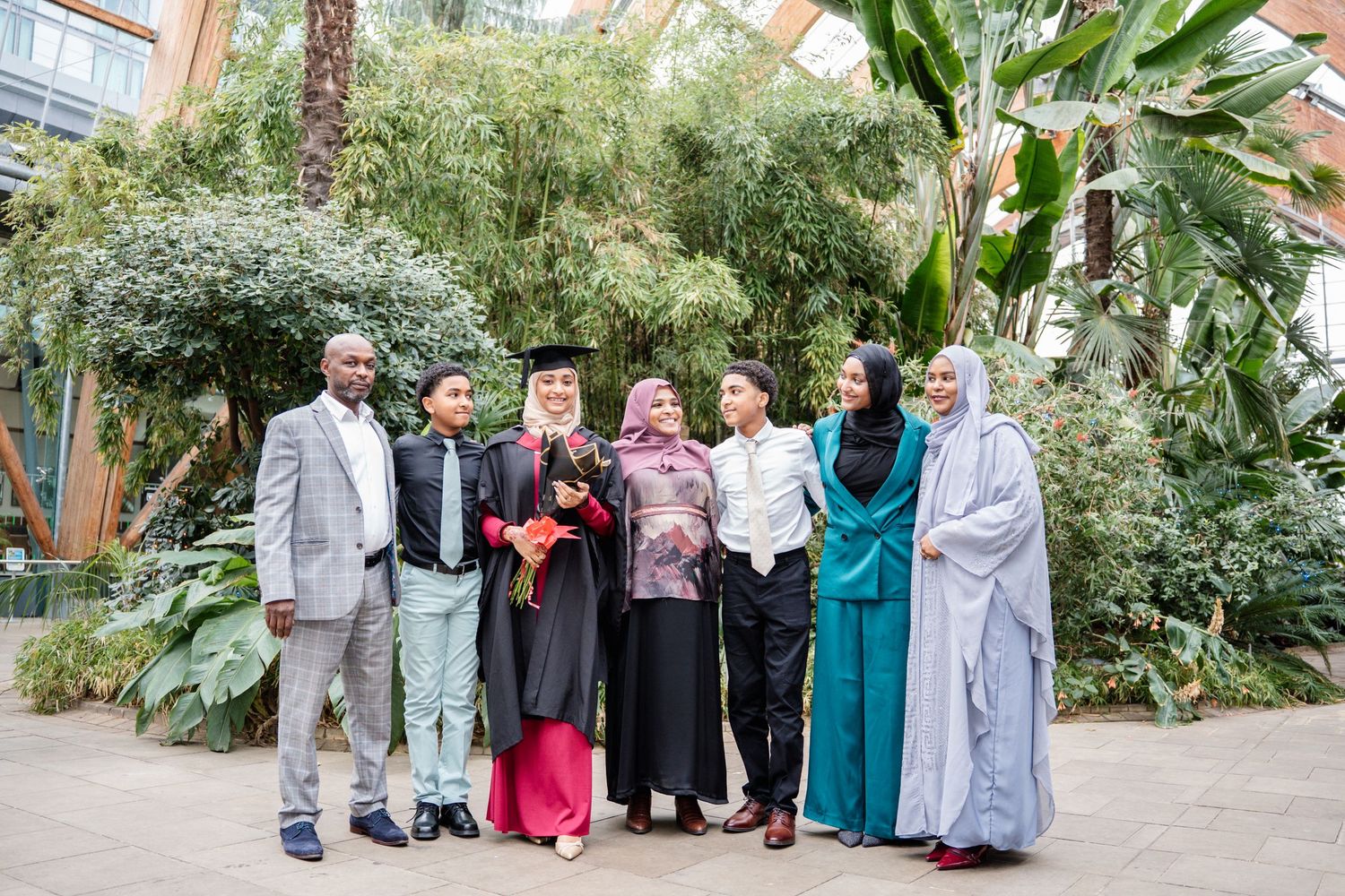 Large group photo of graduates in traditional dress and academic regalia outdoors.