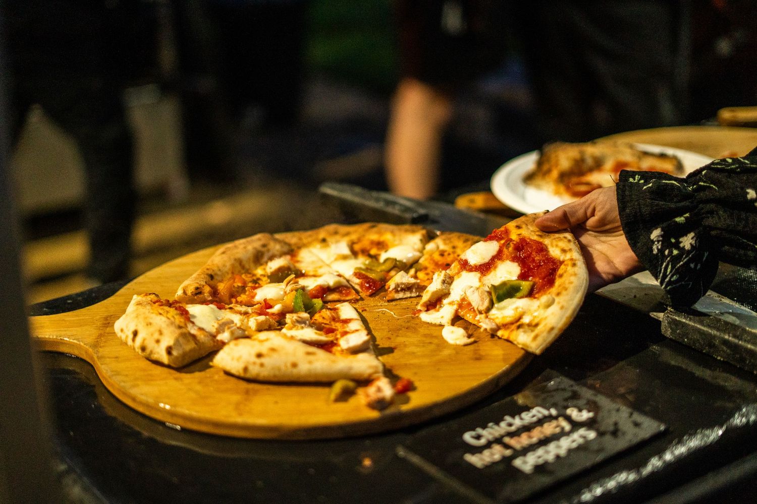 Artisanal pizza with toppings served on a wooden board in dim lighting.