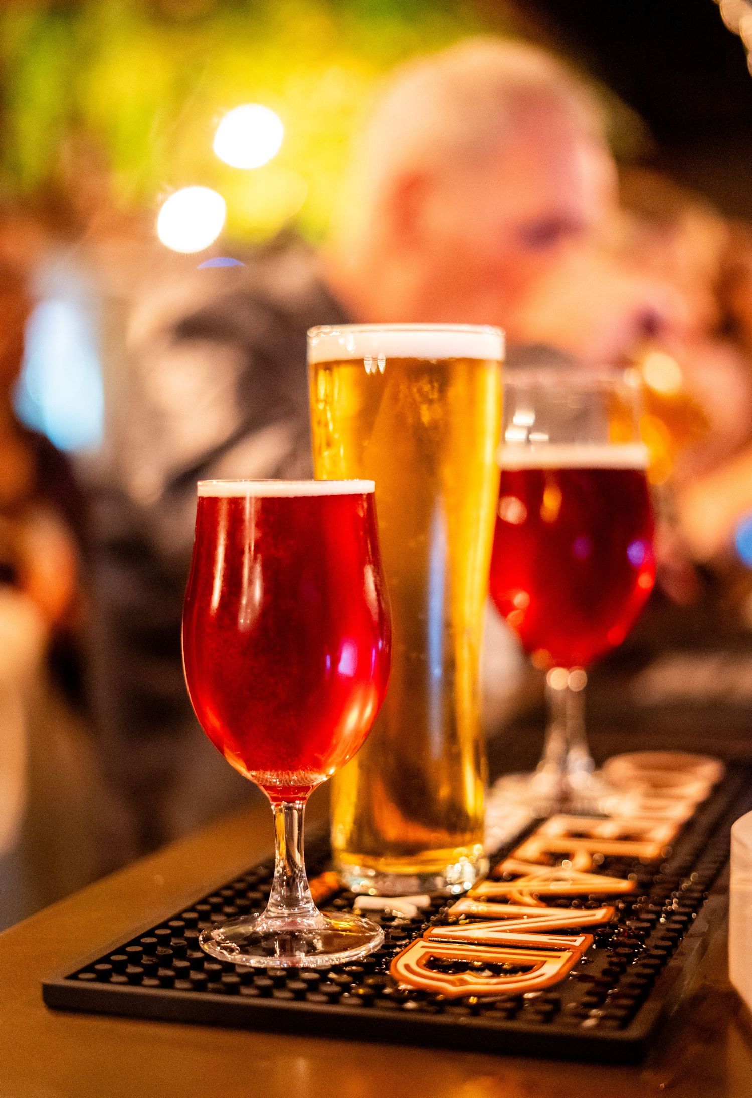 Variety of craft beers including red ale and lager displayed on bar mat with bokeh lighting.