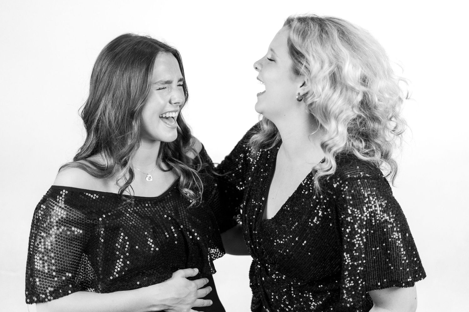 Black and white photo of two performers in sequined outfits sharing laughs during a shoot.