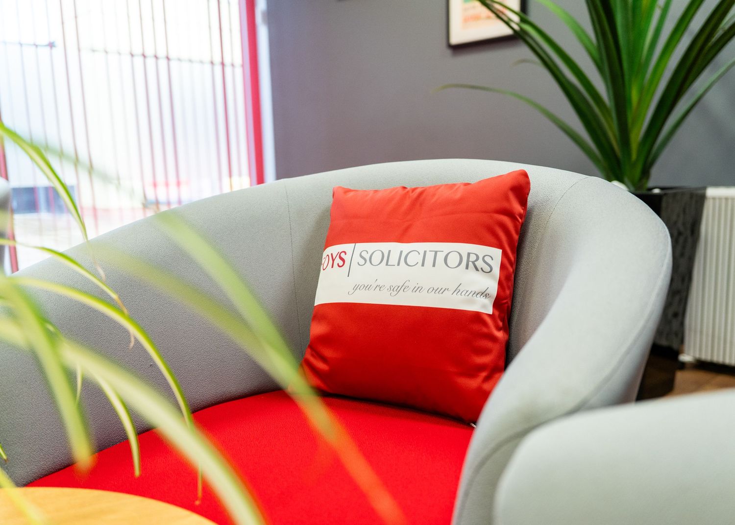 Modern office waiting area with red accent pillows and indoor plants.
