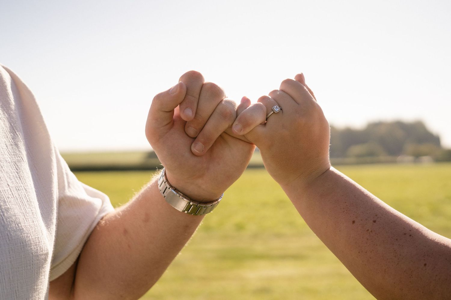 Close-up of intertwined hands against a bright, sunlit background.