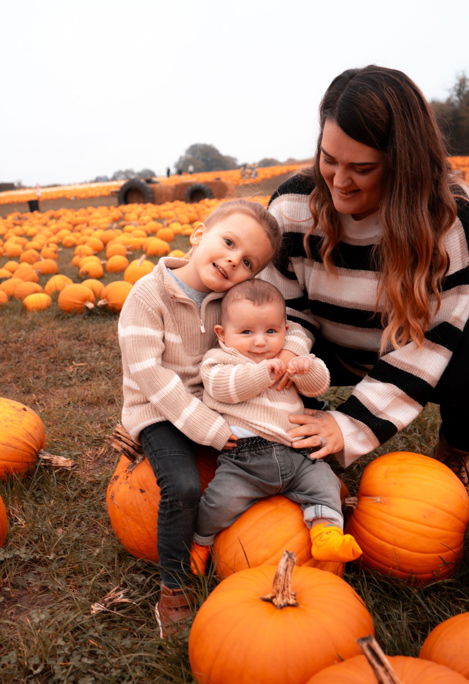 Candid moments captured sitting among large orange pumpkins in a field.