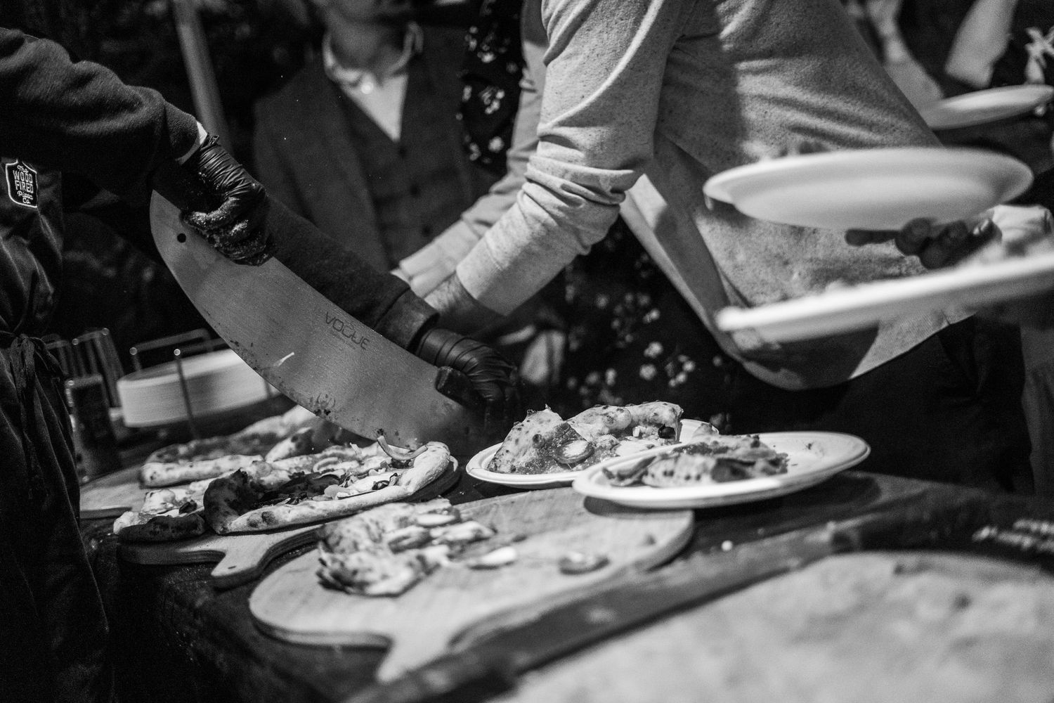 Black and white image of pizzas being served on wooden boards.