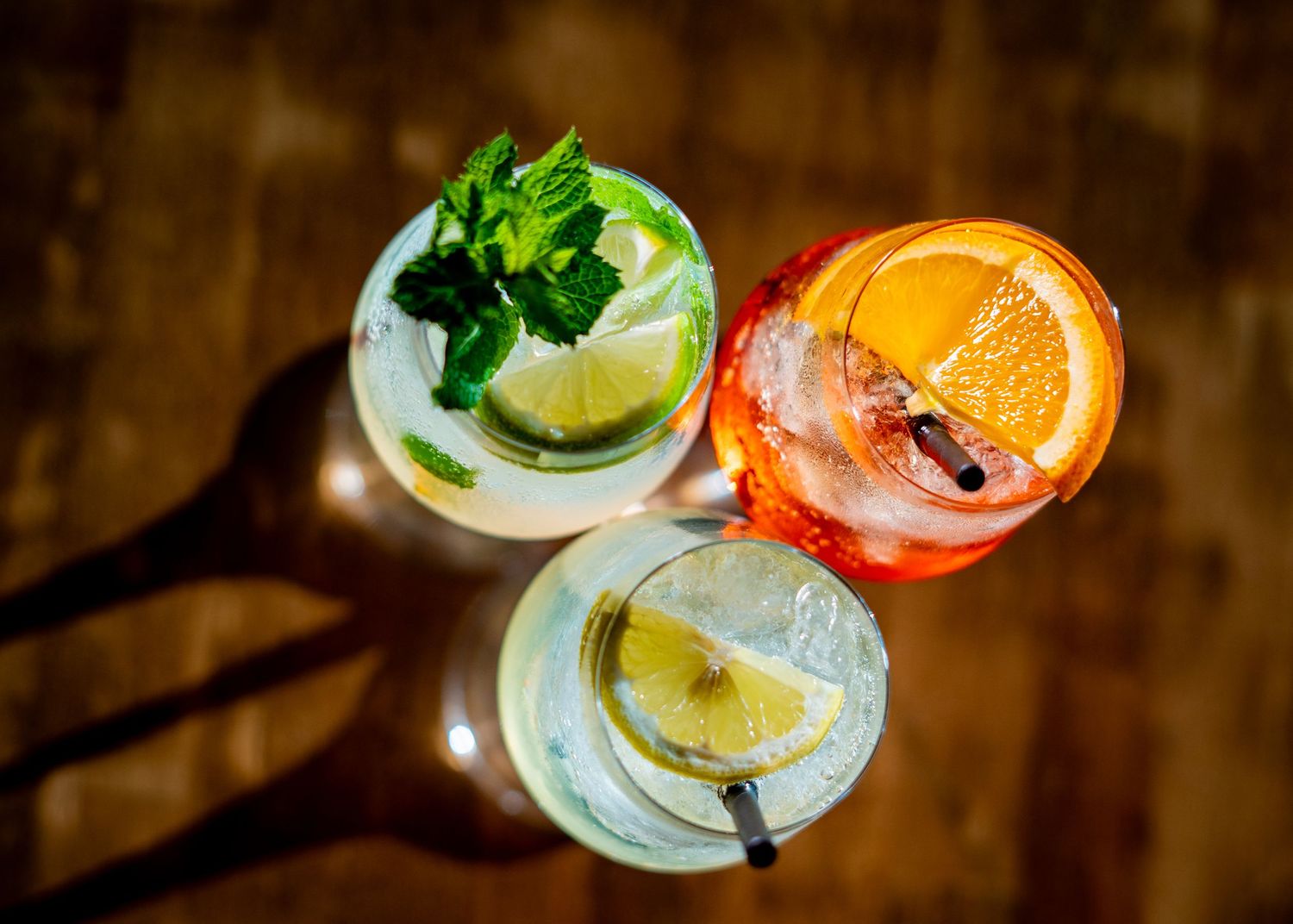 Overhead view of garnished cocktails with fresh herbs and citrus slices.