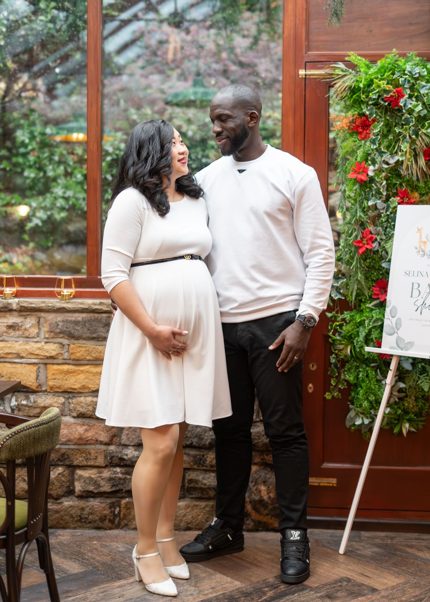 Baby shower celebration in a sunlit conservatory with decorative signage and floral accents.