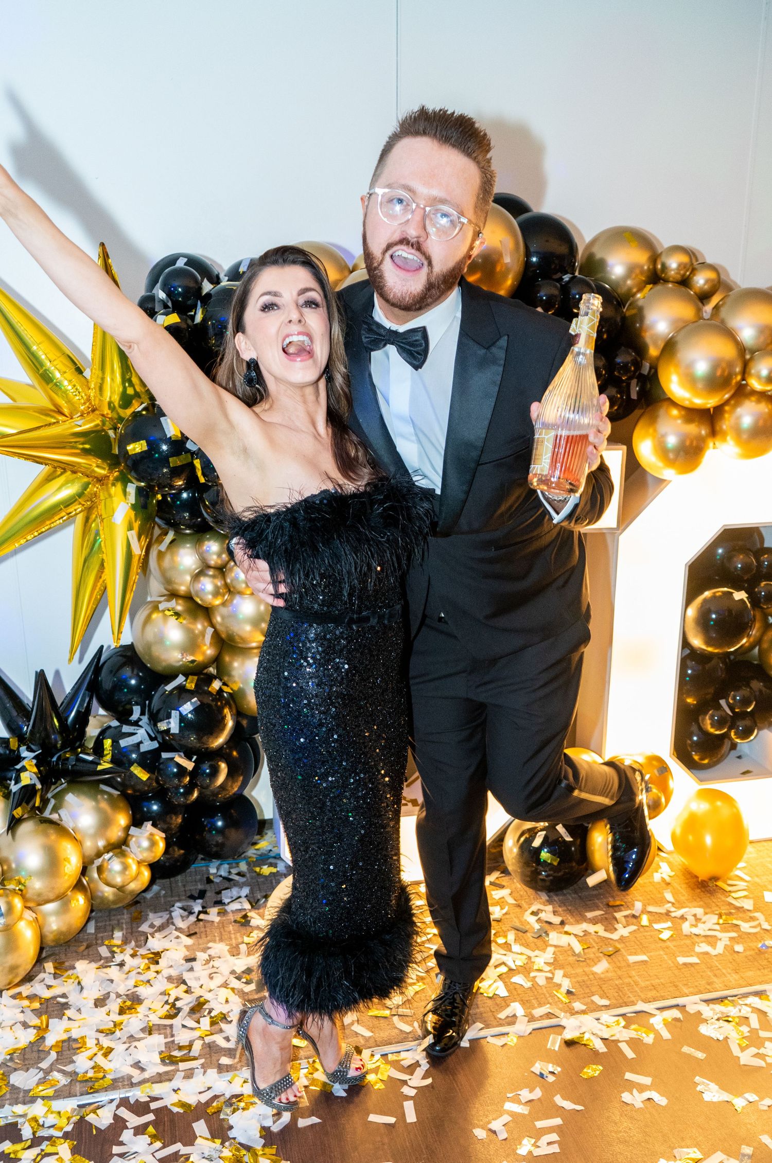 Party scene with gold balloons, confetti and formal attire against white backdrop.