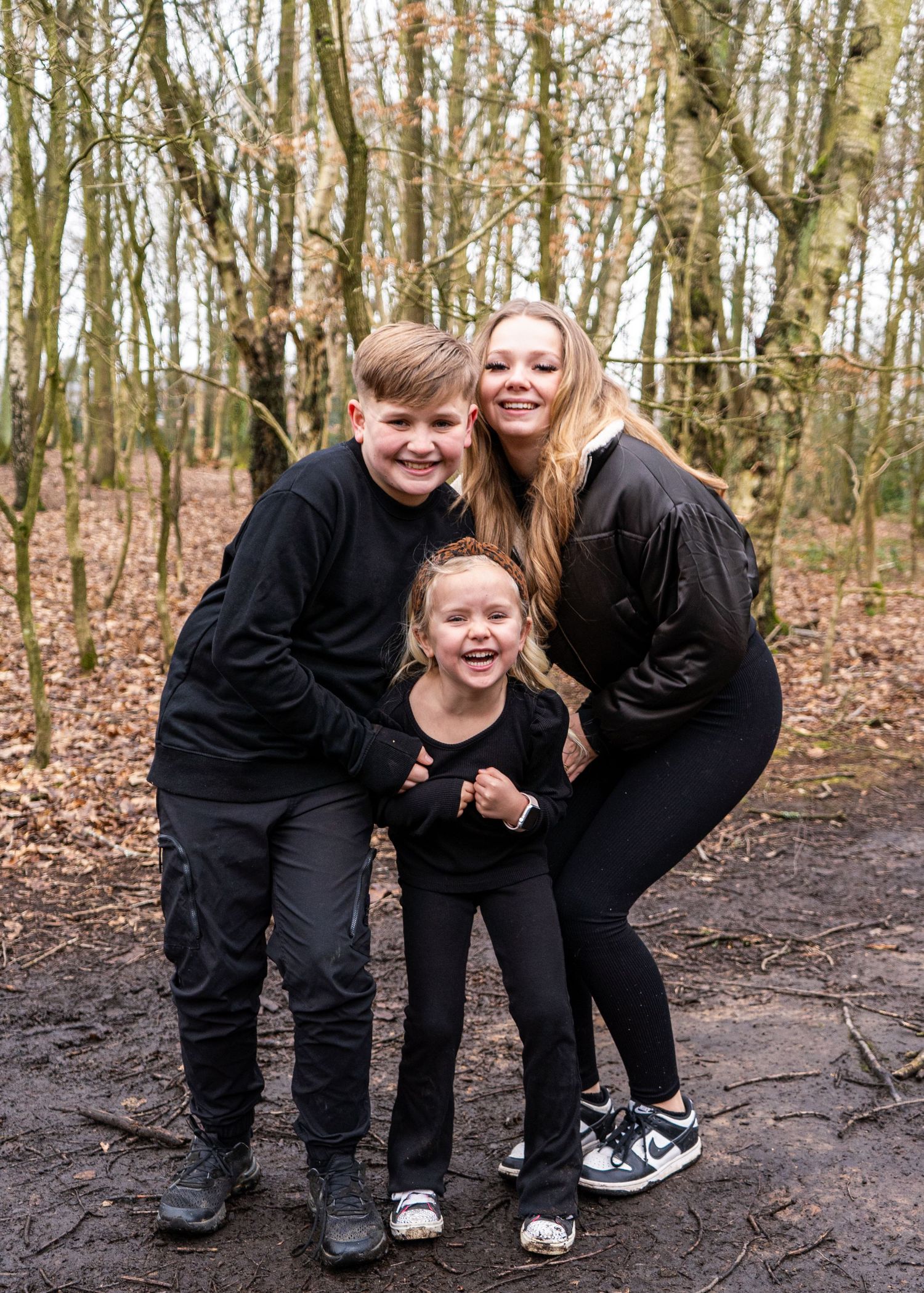 Family members in coordinated black outfits sharing laughs during an outdoor photo session.