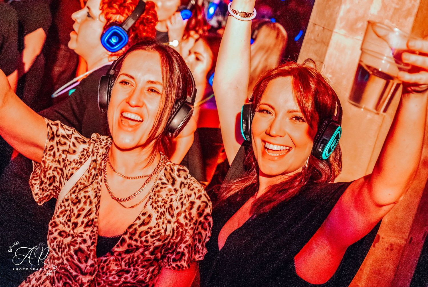 Crowd of partygoers celebrating under warm red lighting at a nightclub event.