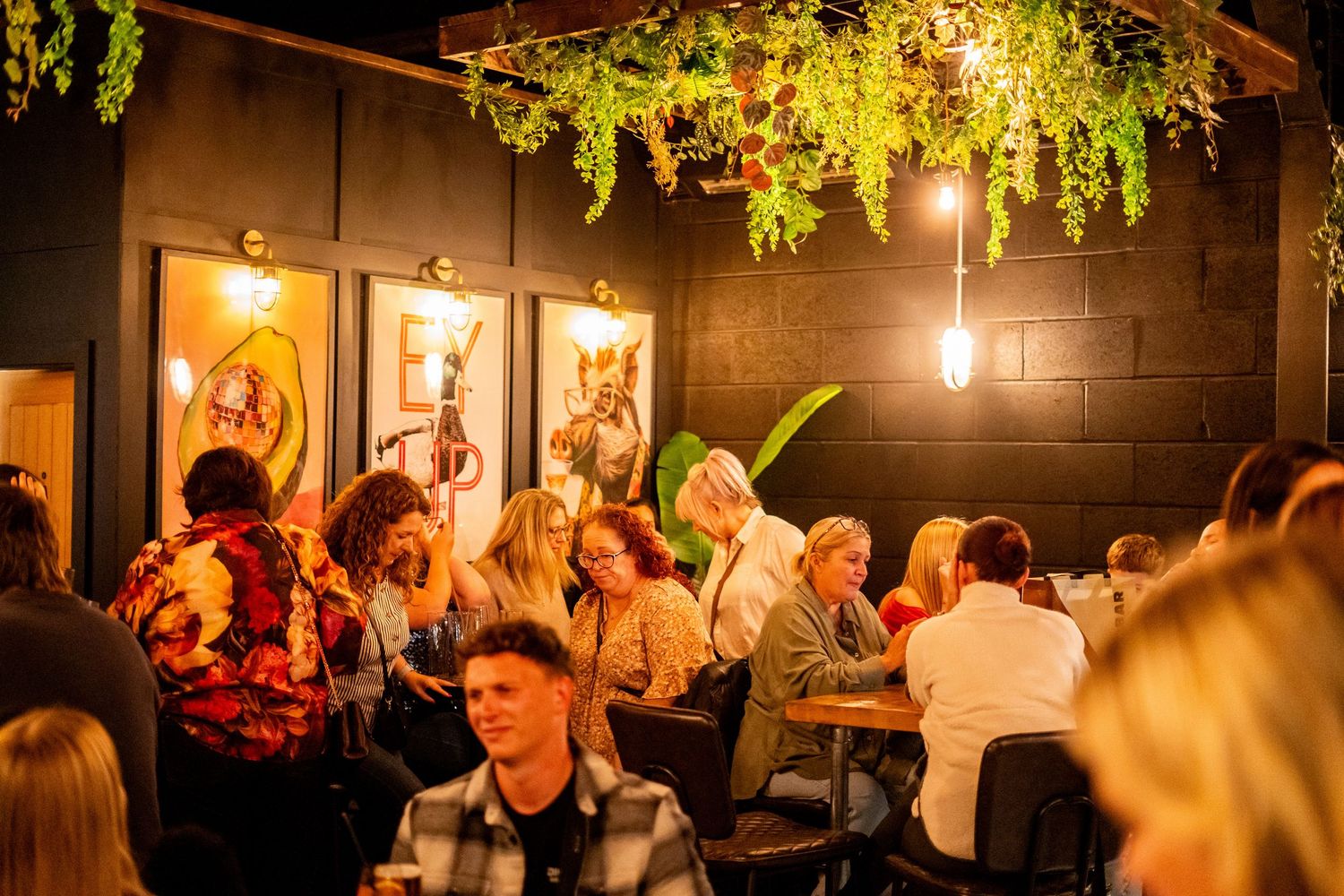 Bustling restaurant interior with hanging plants and warm lighting creating vibrant atmosphere.