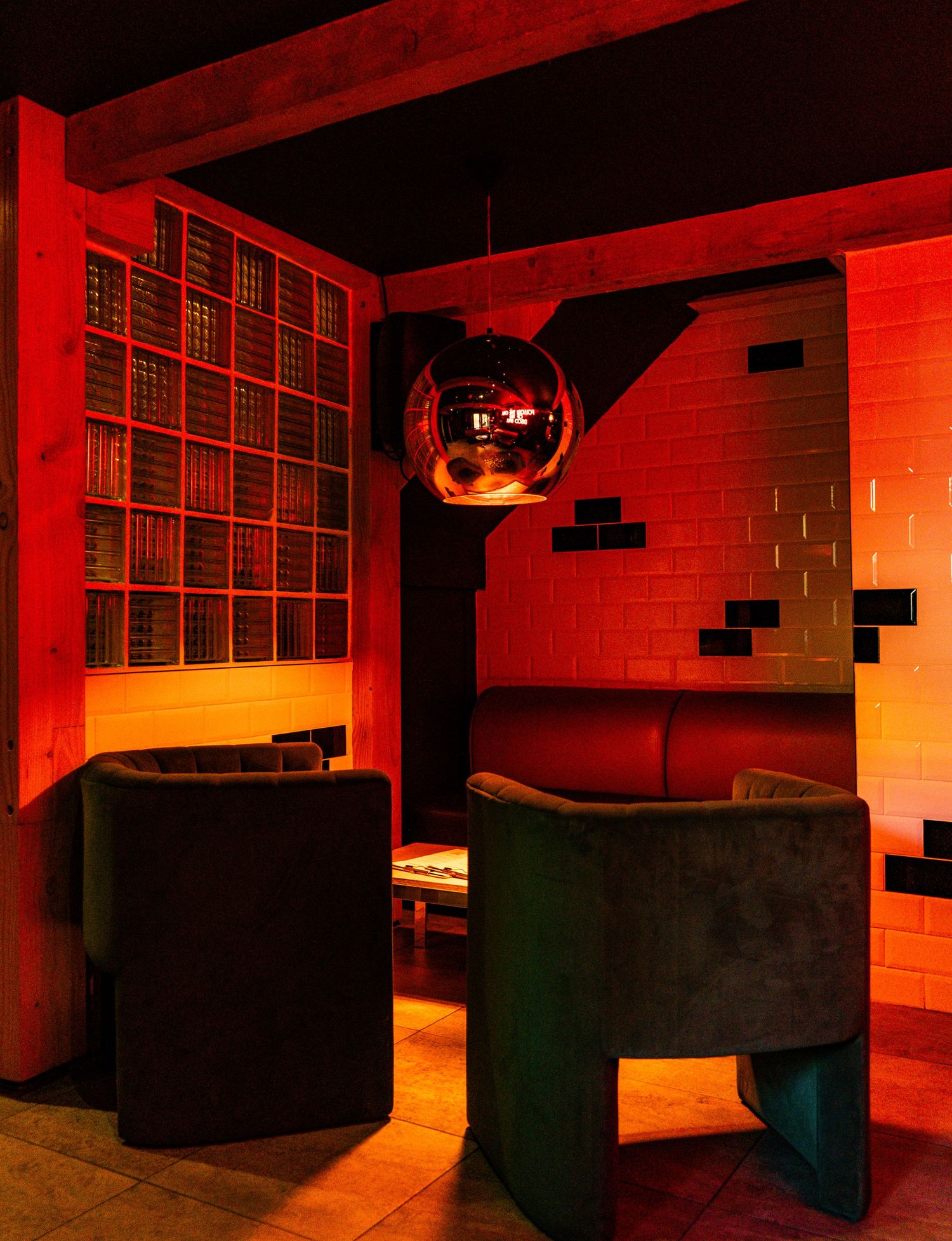 Modern lounge area with spherical disco ball and black seating under dramatic red lighting.