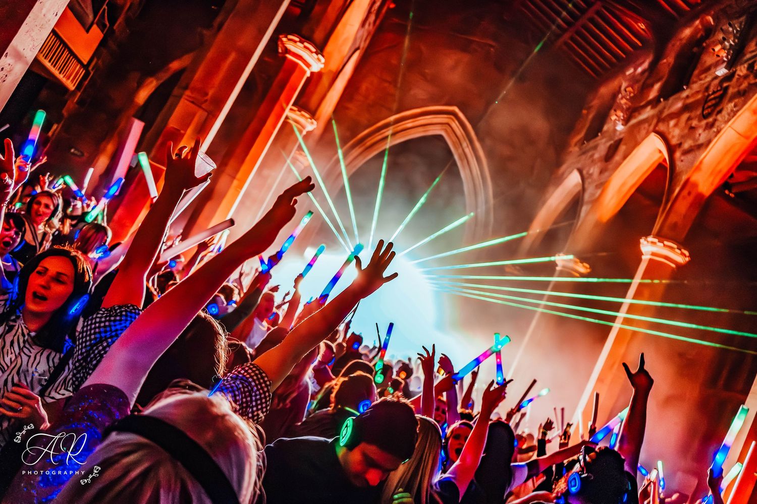 Concert crowd with raised hands silhouetted against bright red stage lighting.