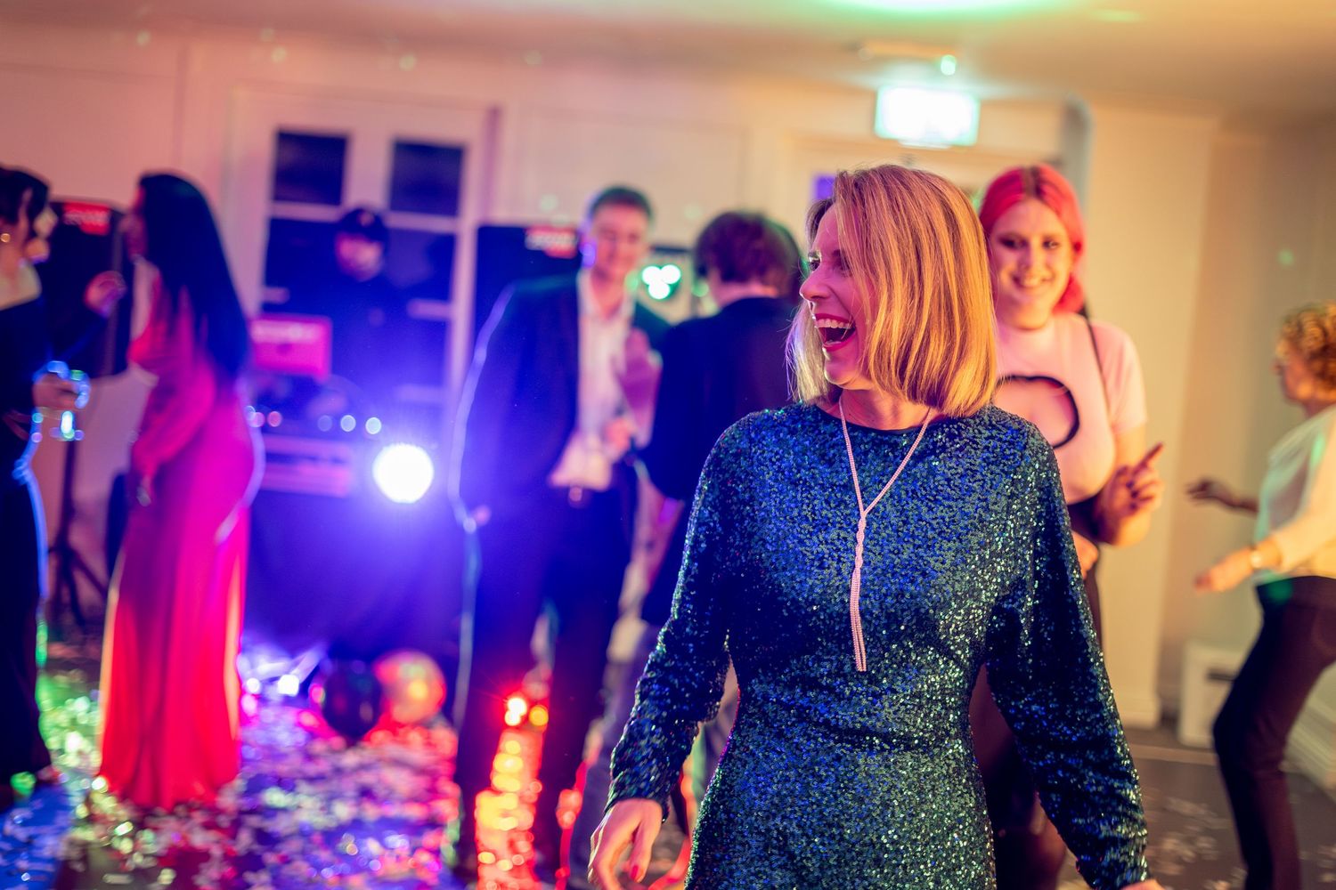 Lively indoor celebration with colorful lights and people dancing.