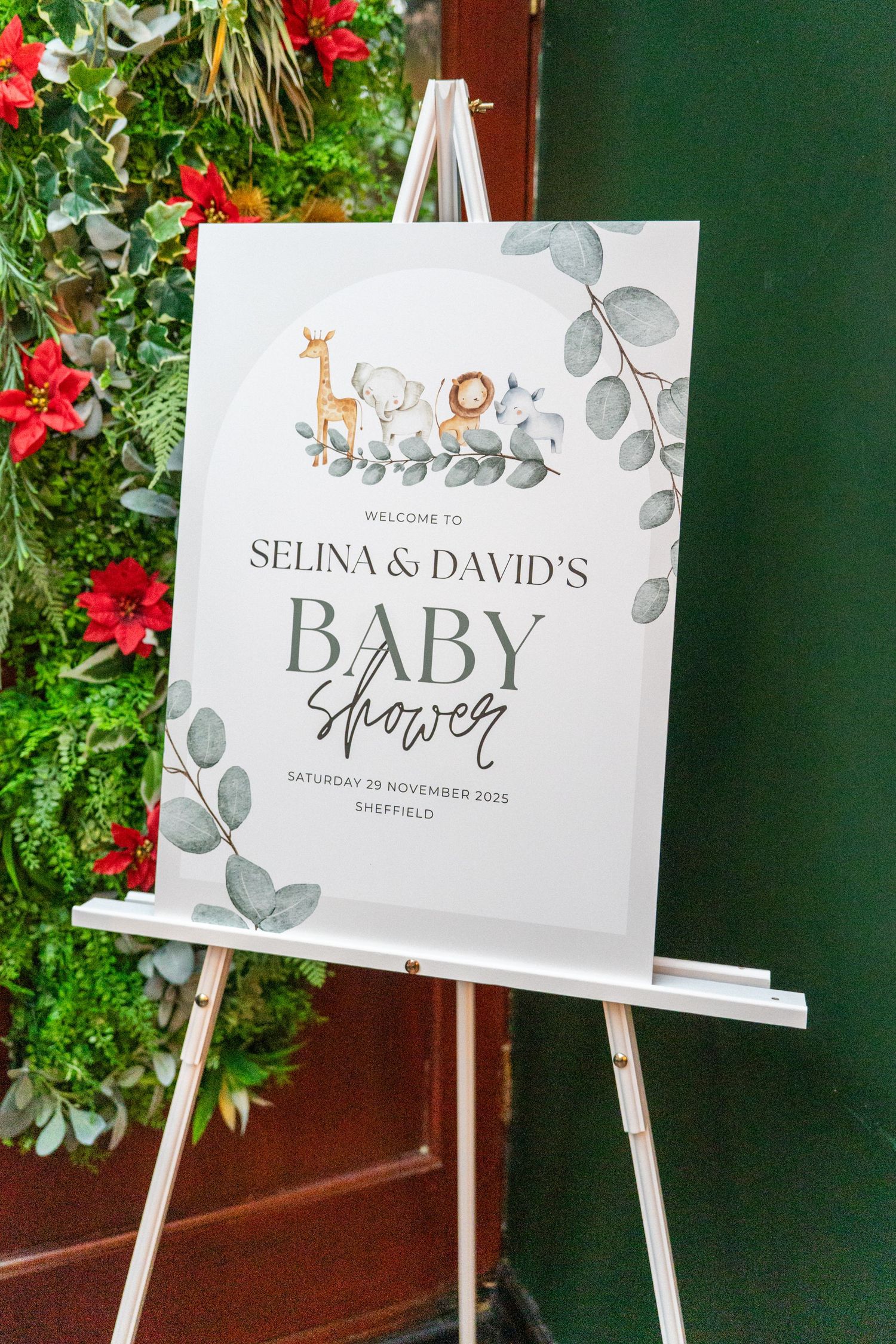Elegant baby shower signage displayed on white easels with eucalyptus leaf designs.