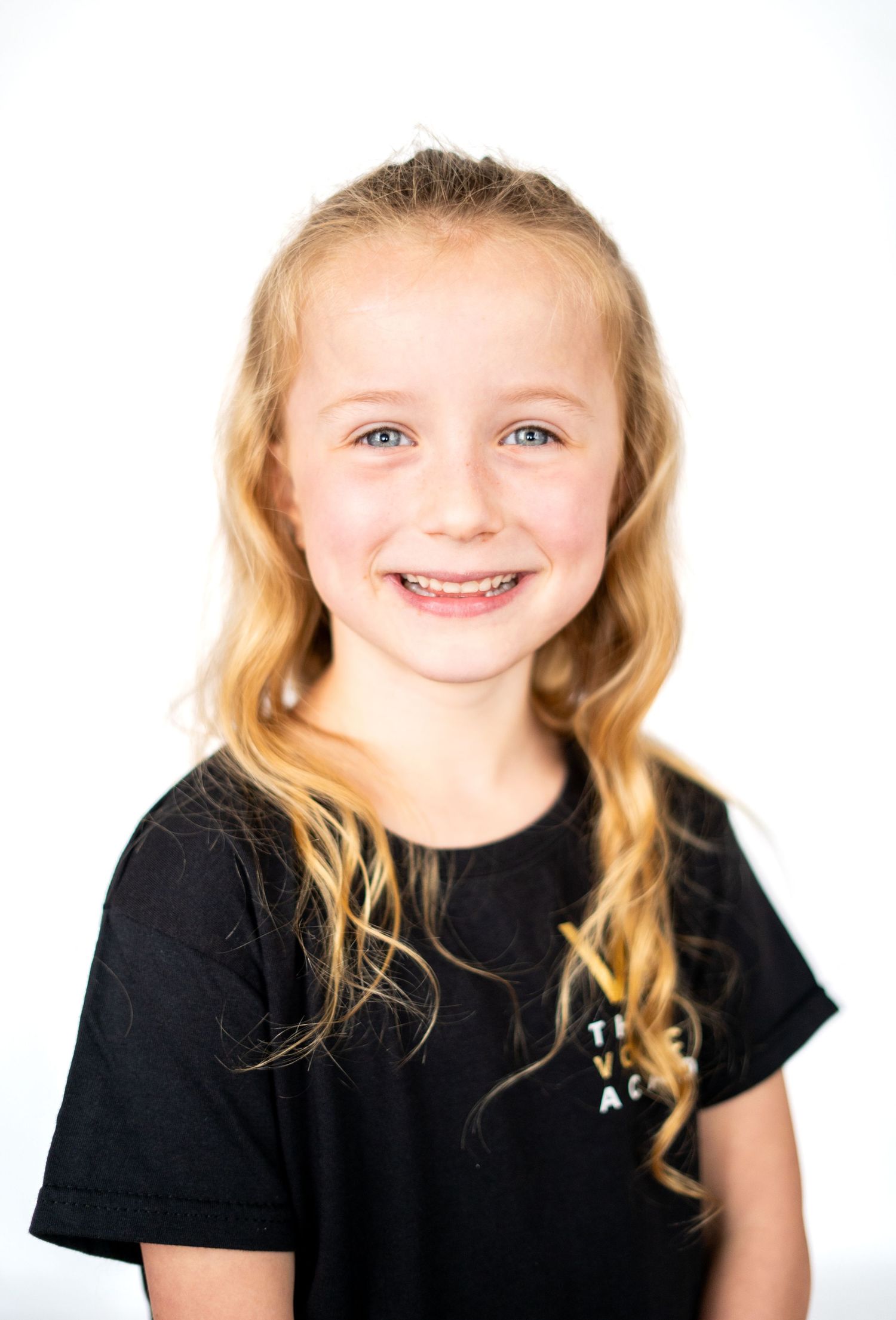 Young person with blonde hair wearing black t-shirt smiling against white background.