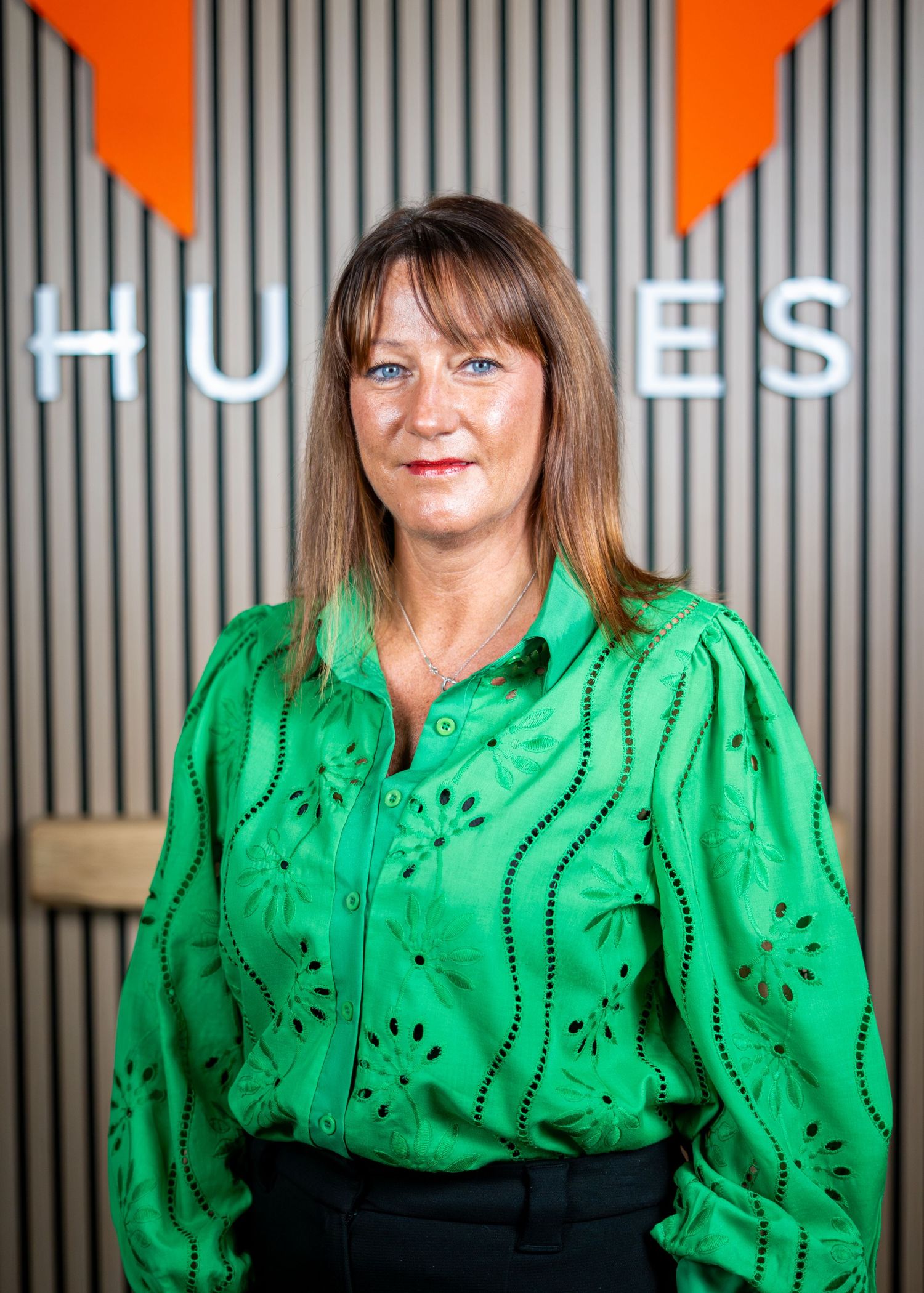 Professional in bright green blouse poses against modern office wall with orange accents.