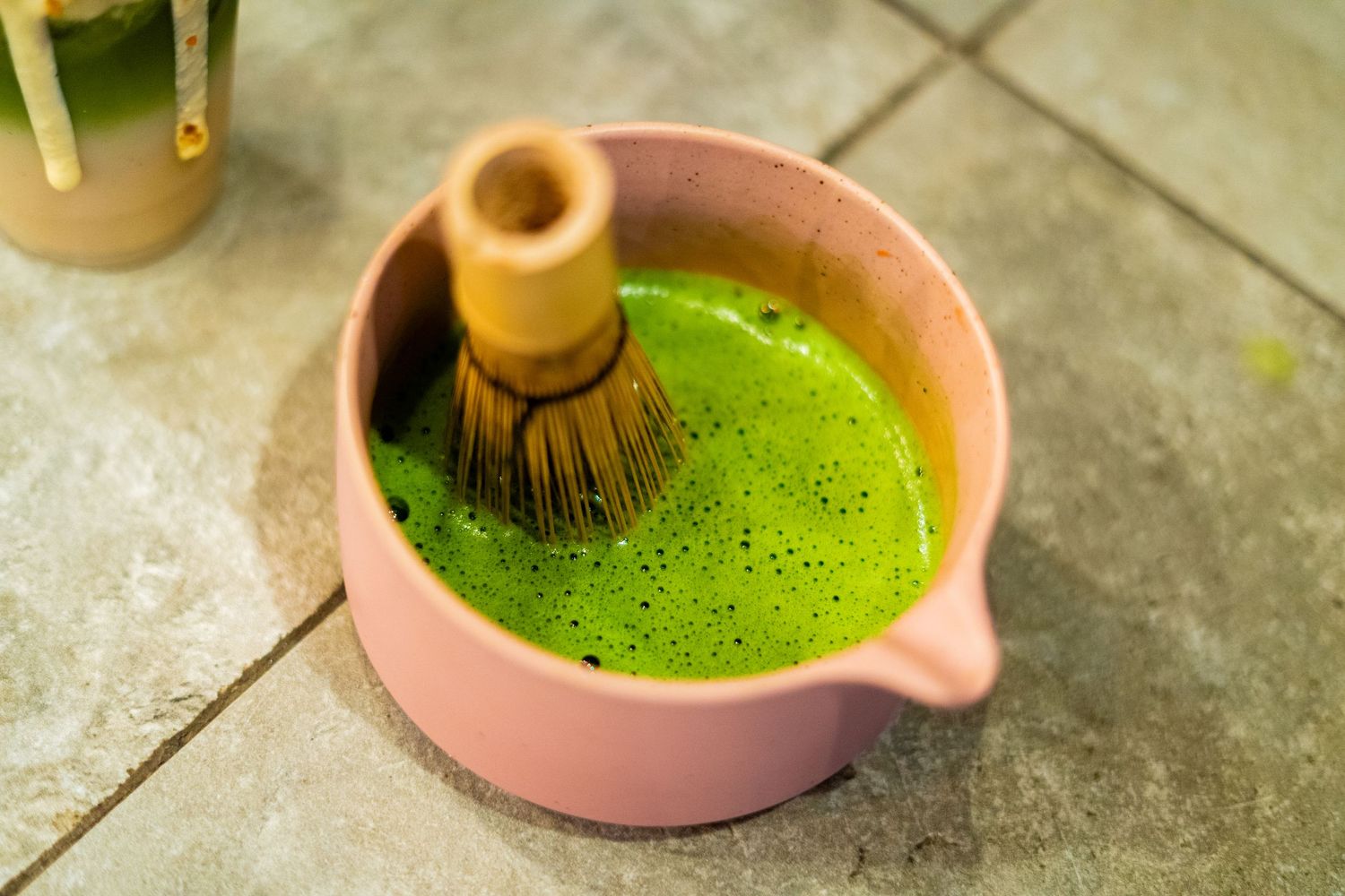 Green matcha tea being prepared in a pink ceramic bowl.