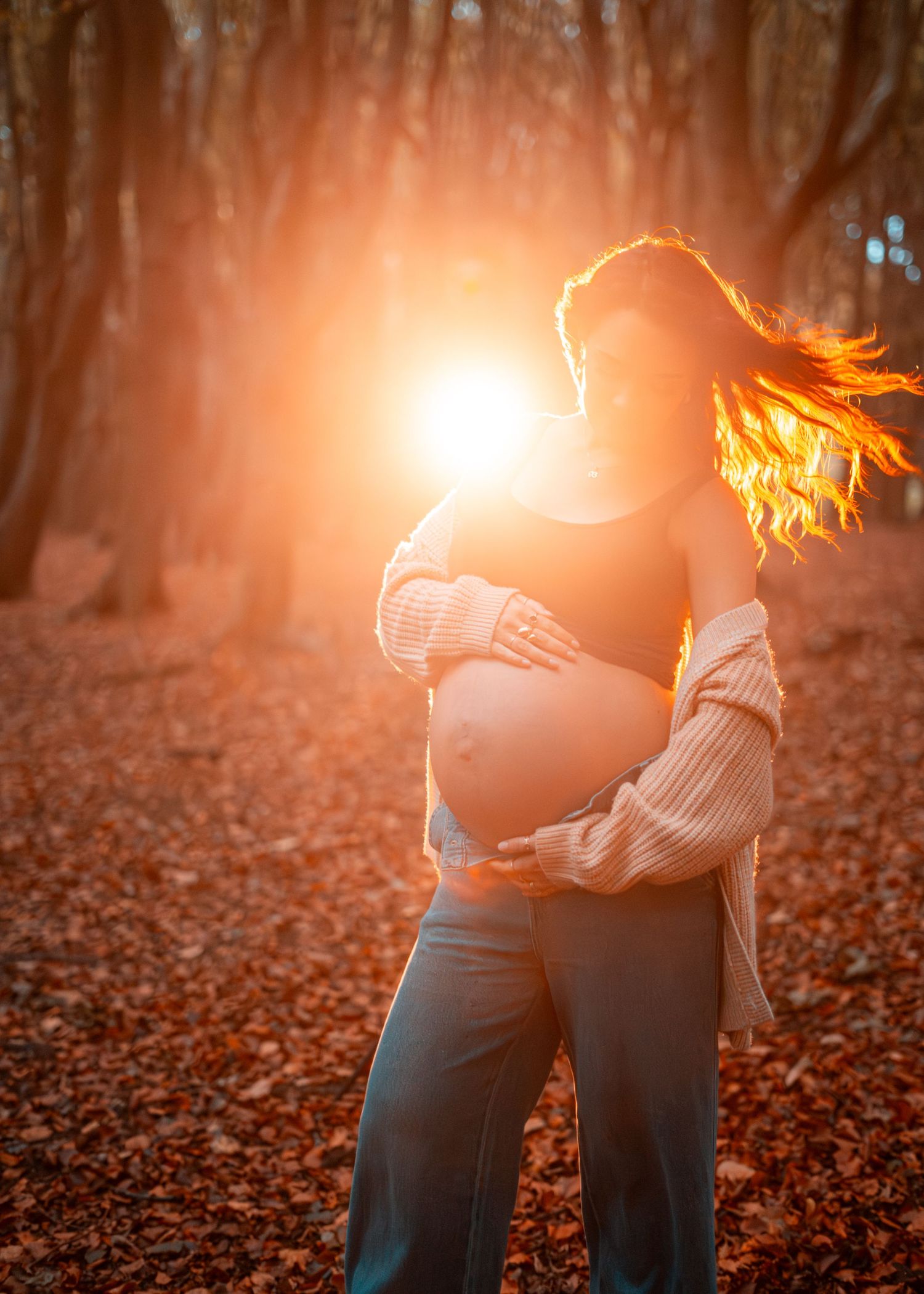 Dramatic sunset lighting illuminates figure among fallen autumn leaves in wooded setting.