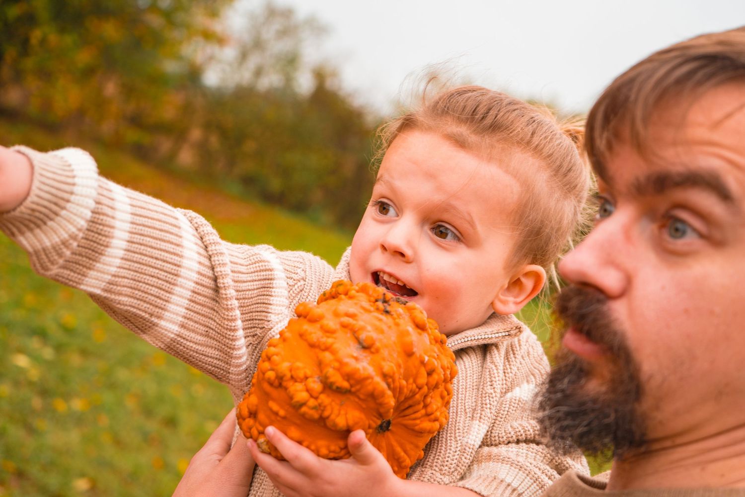 Family shares playful moments with pumpkins in an autumn field during a fall photoshoot.