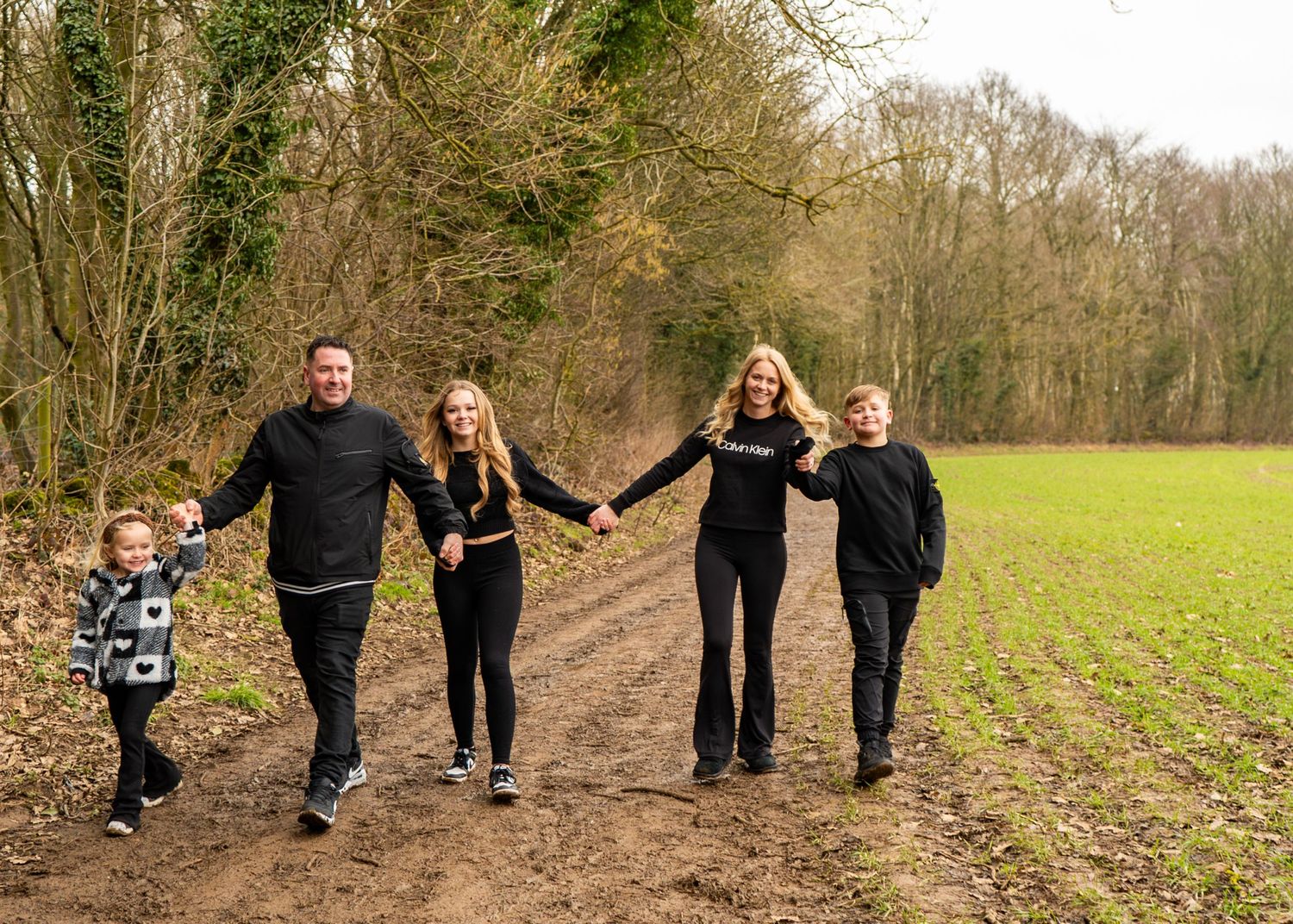 A family walking together on a dirt path through a wooded area.