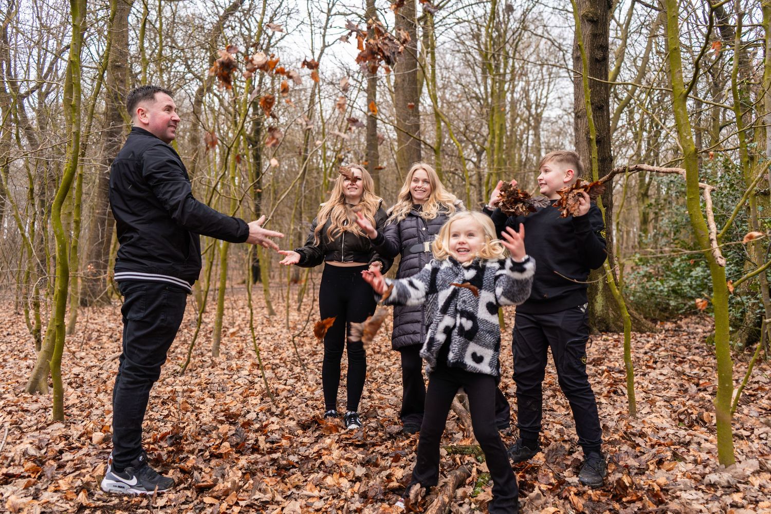 A playful group throws leaves in the air while enjoying an autumn day in the woods.