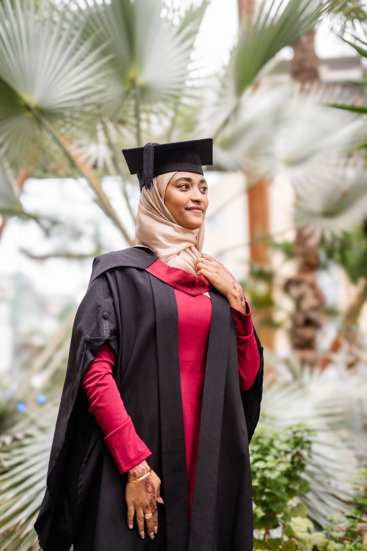 Candid graduation photos captured through tropical plants in greenhouse setting.