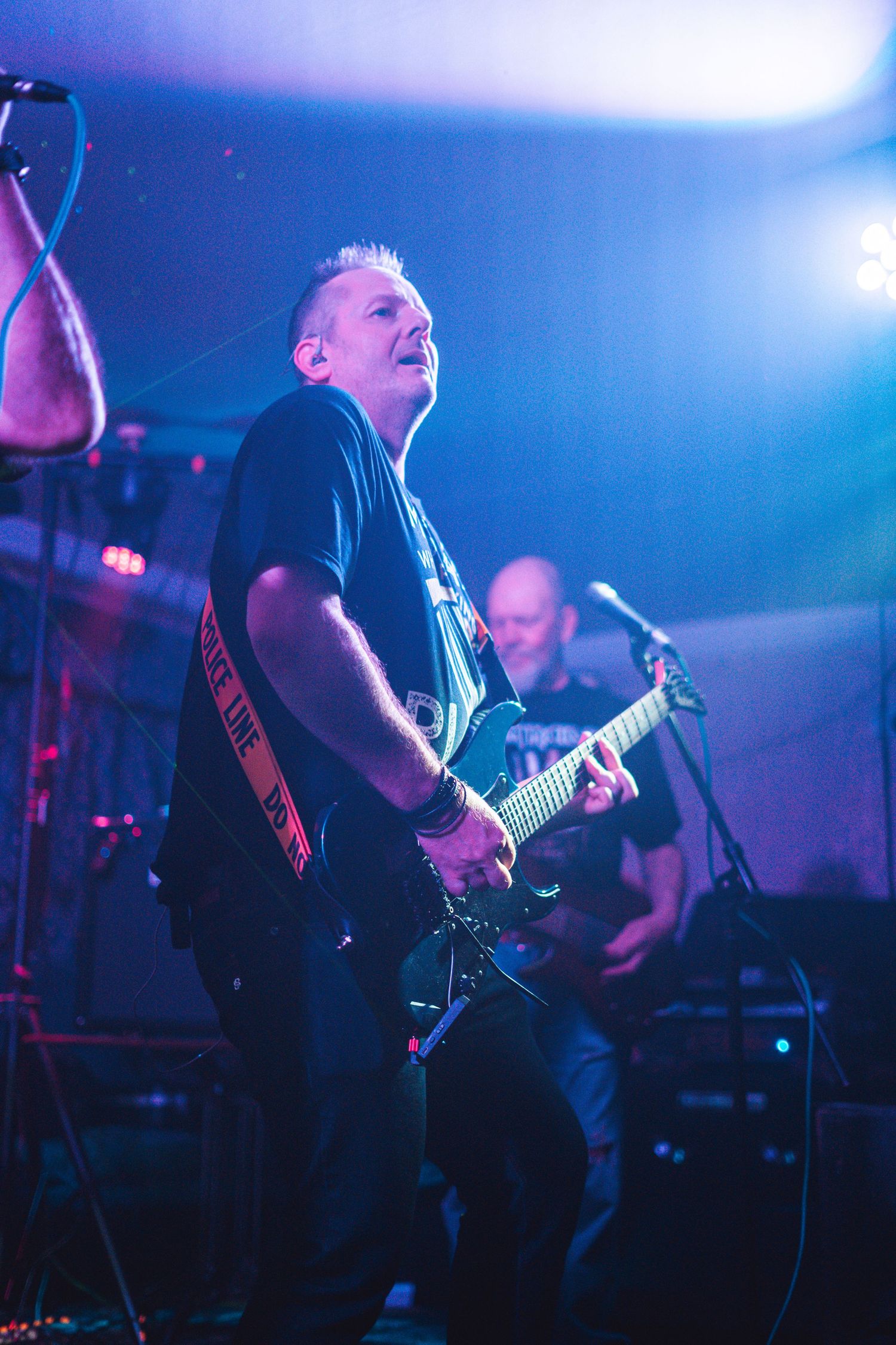 Musician plays electric guitar on stage illuminated by blue concert lighting.