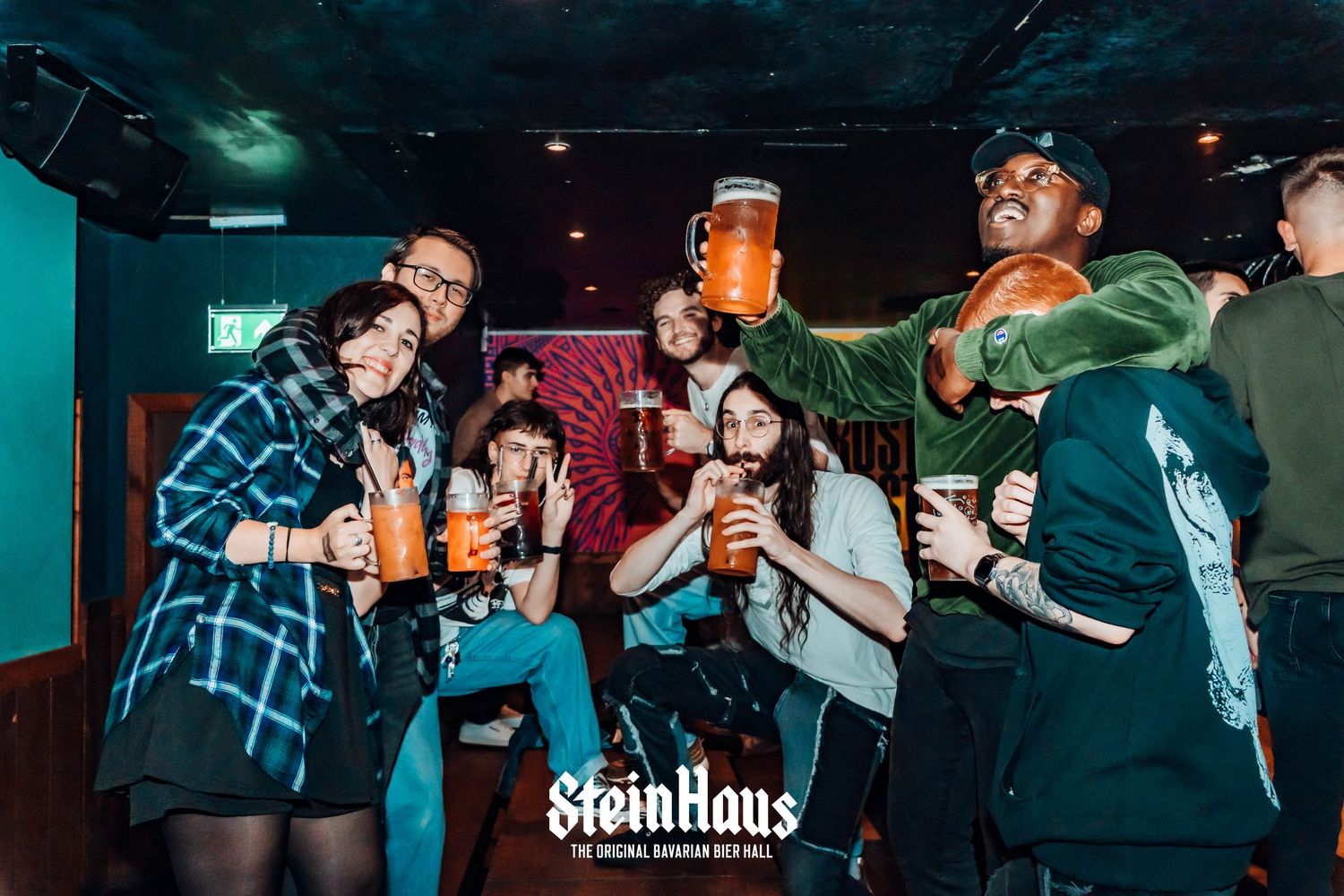 Partygoers raising beer glasses in a dark bar with ambient lighting.