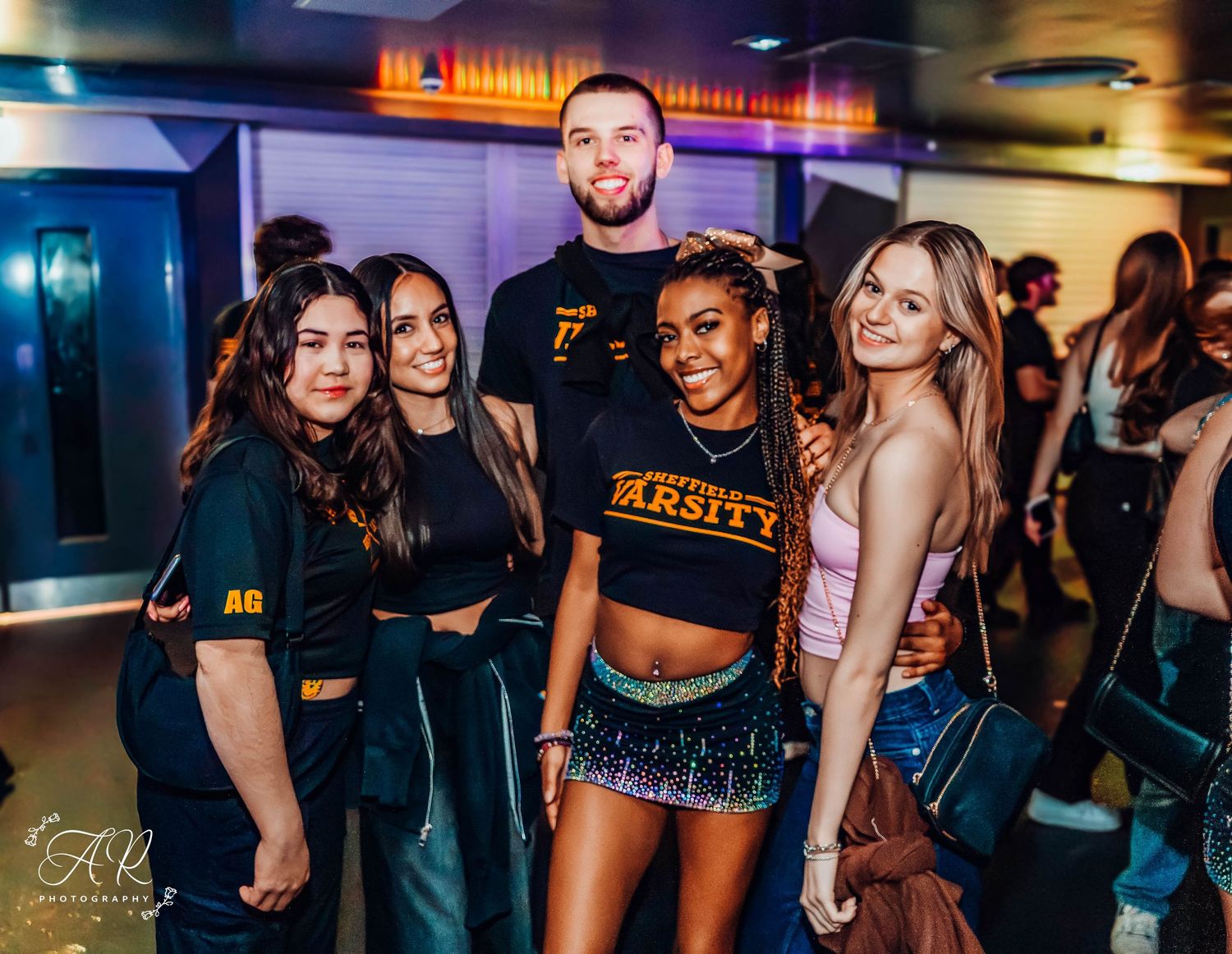 Friends in matching black shirts posing together at a nightclub with blue lighting effects.
