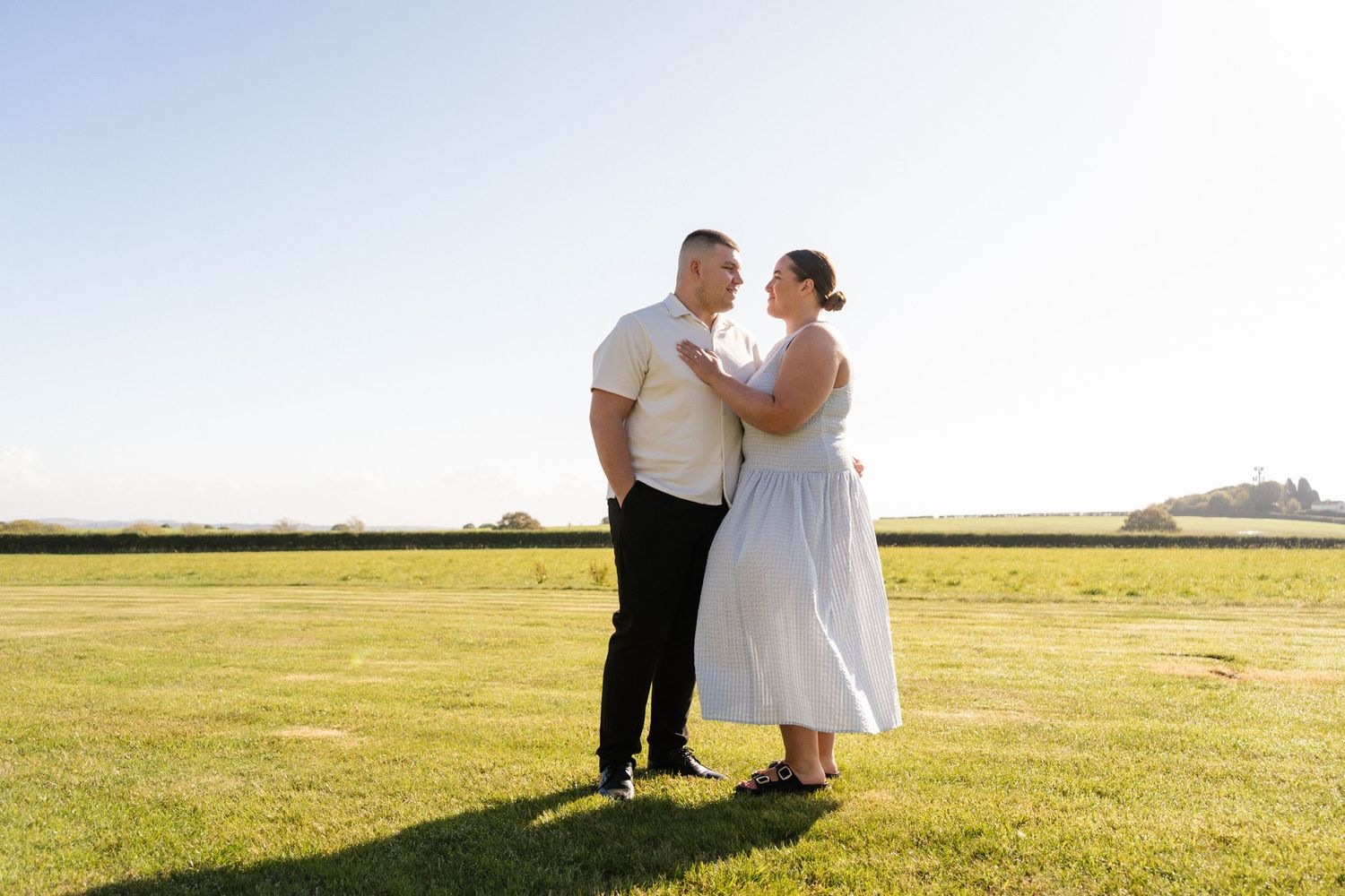 A couple shares a romantic moment in a sun-drenched field at golden hour.