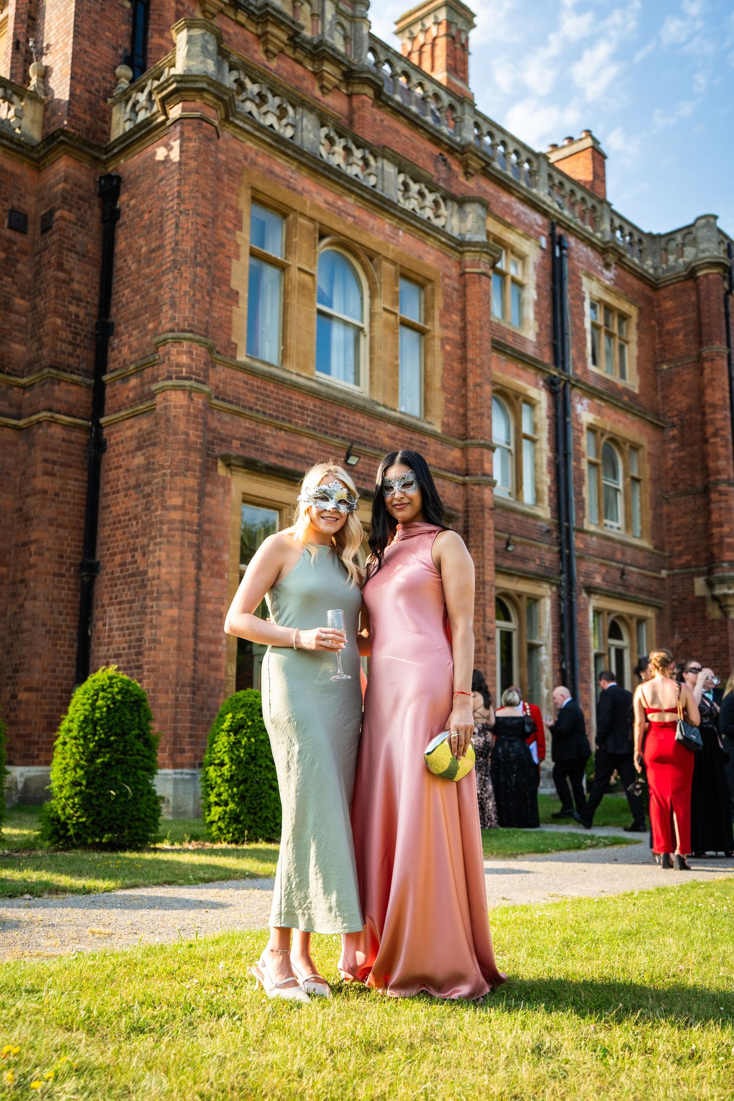 Wedding guests enjoying a sunny afternoon on the lawn of a historic brick manor house.