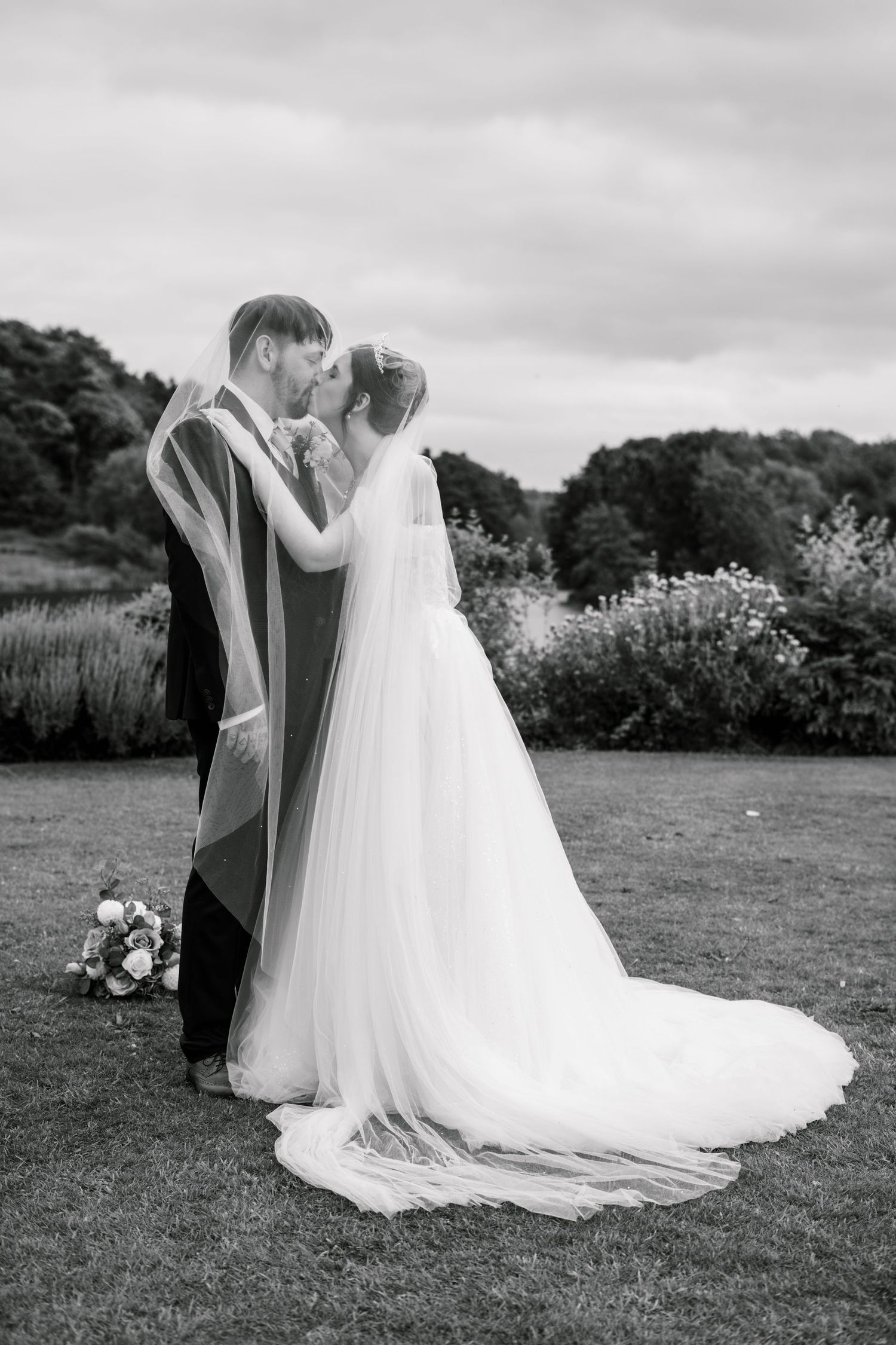 A romantic wedding photoshoot on a grassy lawn with flowing white dress and veil in black and white.