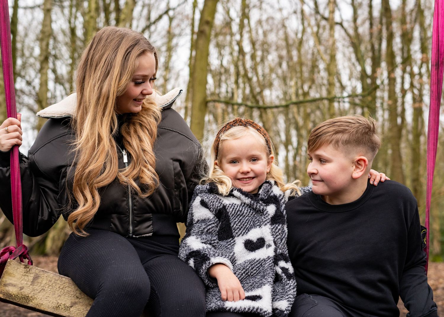 Playful outdoor family portrait with everyone dressed in black against bare winter trees.