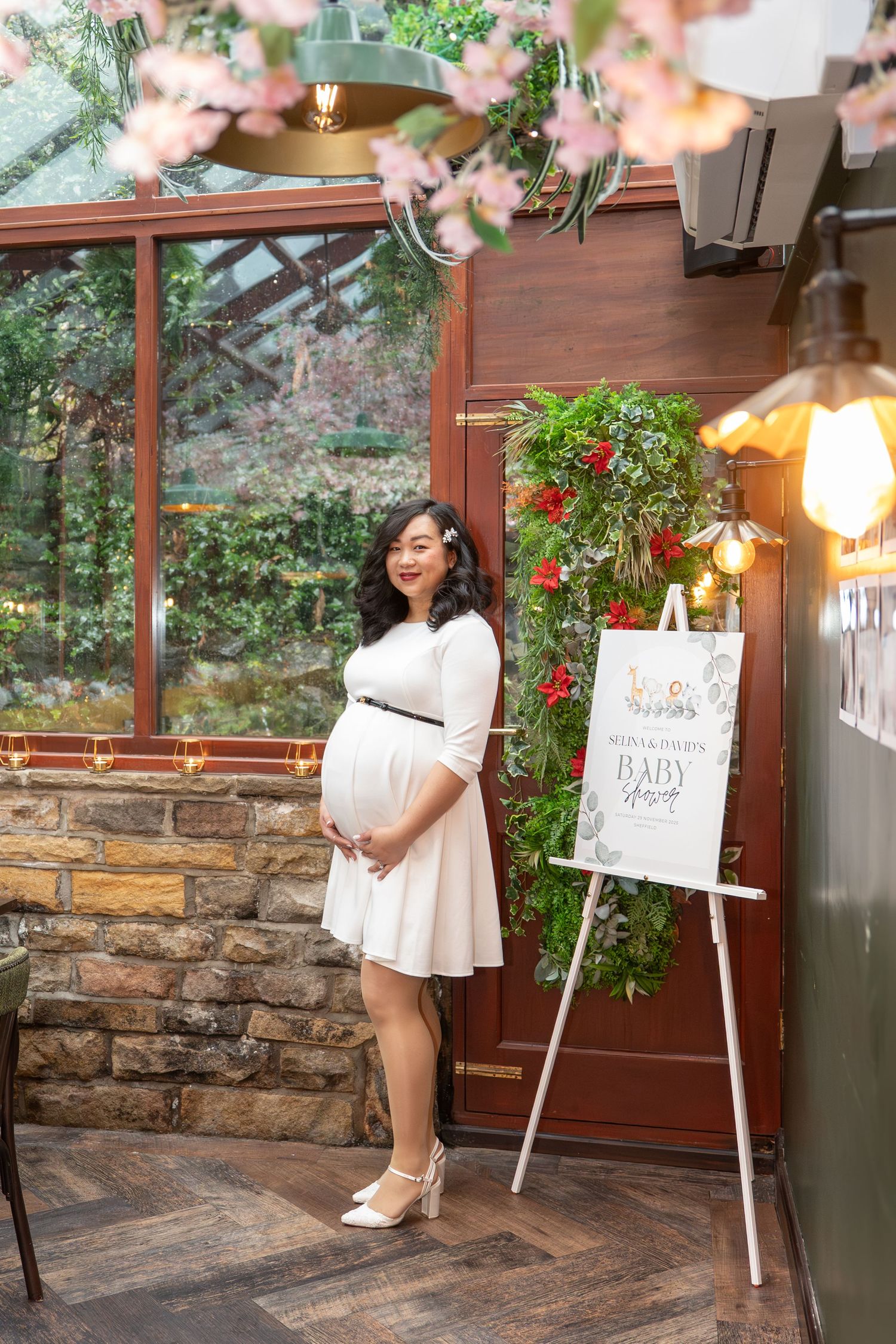 Baby shower celebration in a sunlit venue with white easel signs and floral decorations.
