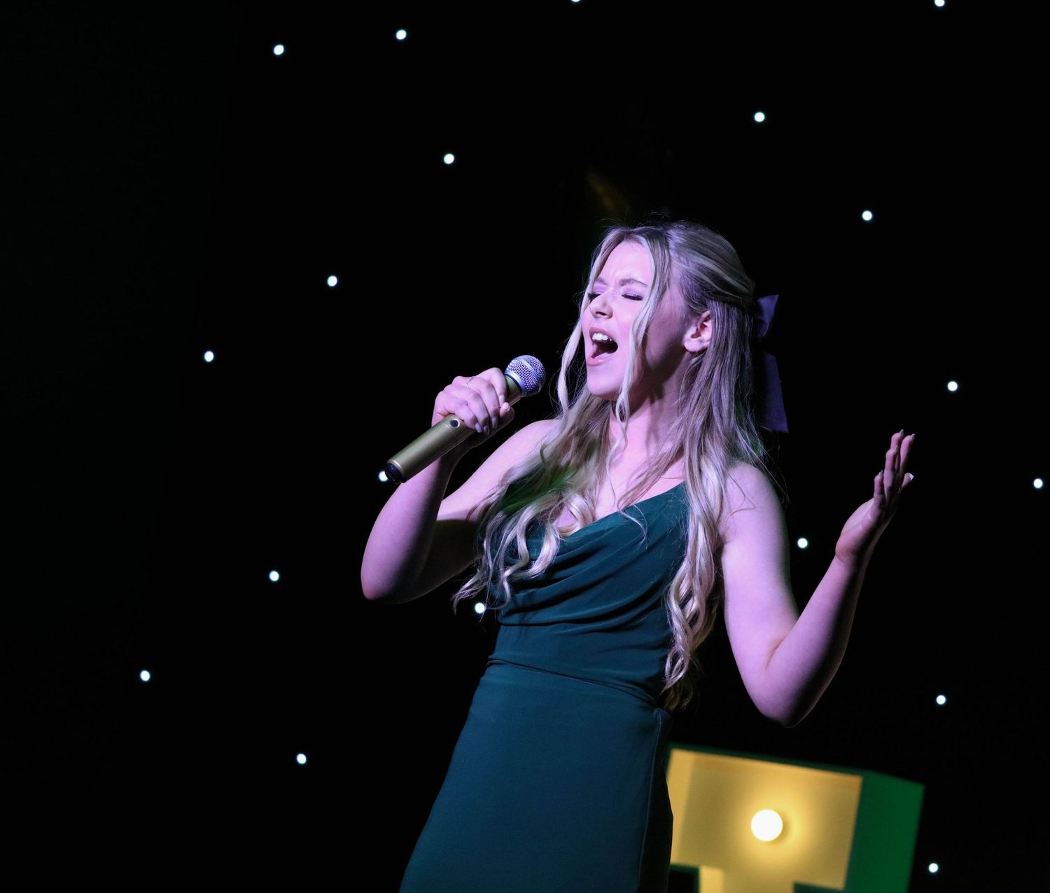 Singer in dark dress performs passionately against starlit backdrop on stage.