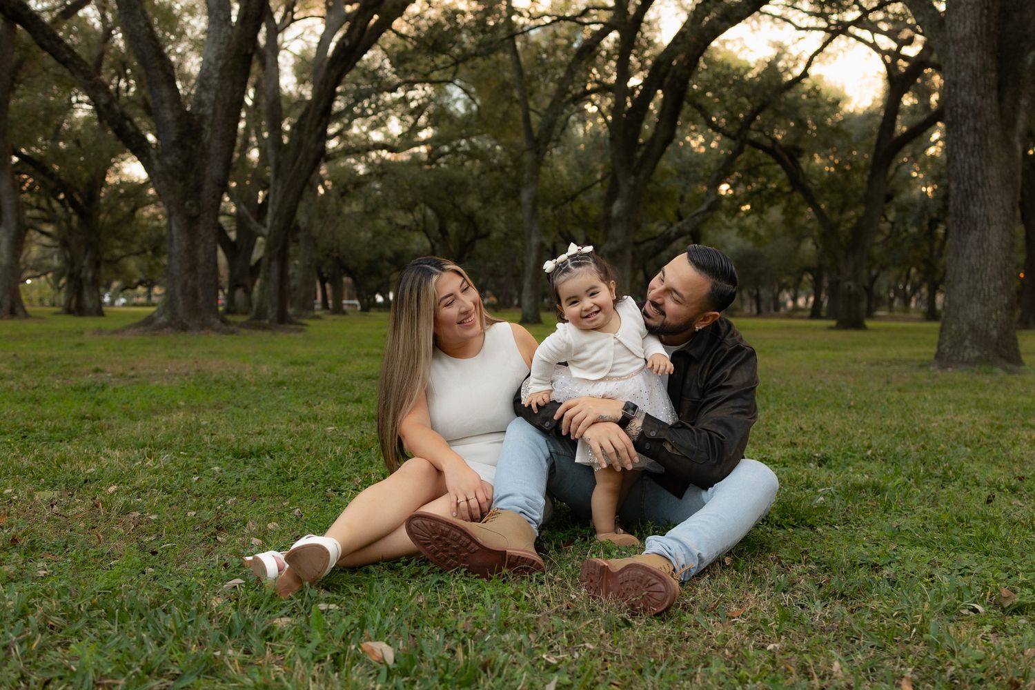 A family sits together on grass in a park during golden hour.